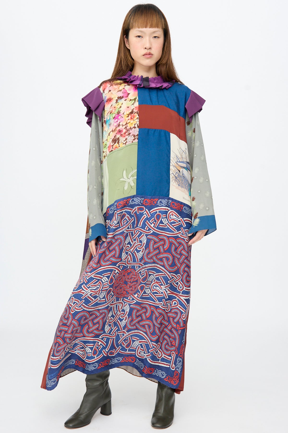A person wearing a Bettina Bakdal Ruffled Collar and Shoulder Dress in Ilse Fehli, a vintage silk dress with floral and Celtic knotwork patterns, a purple ruffled collar, and shoulder accents.