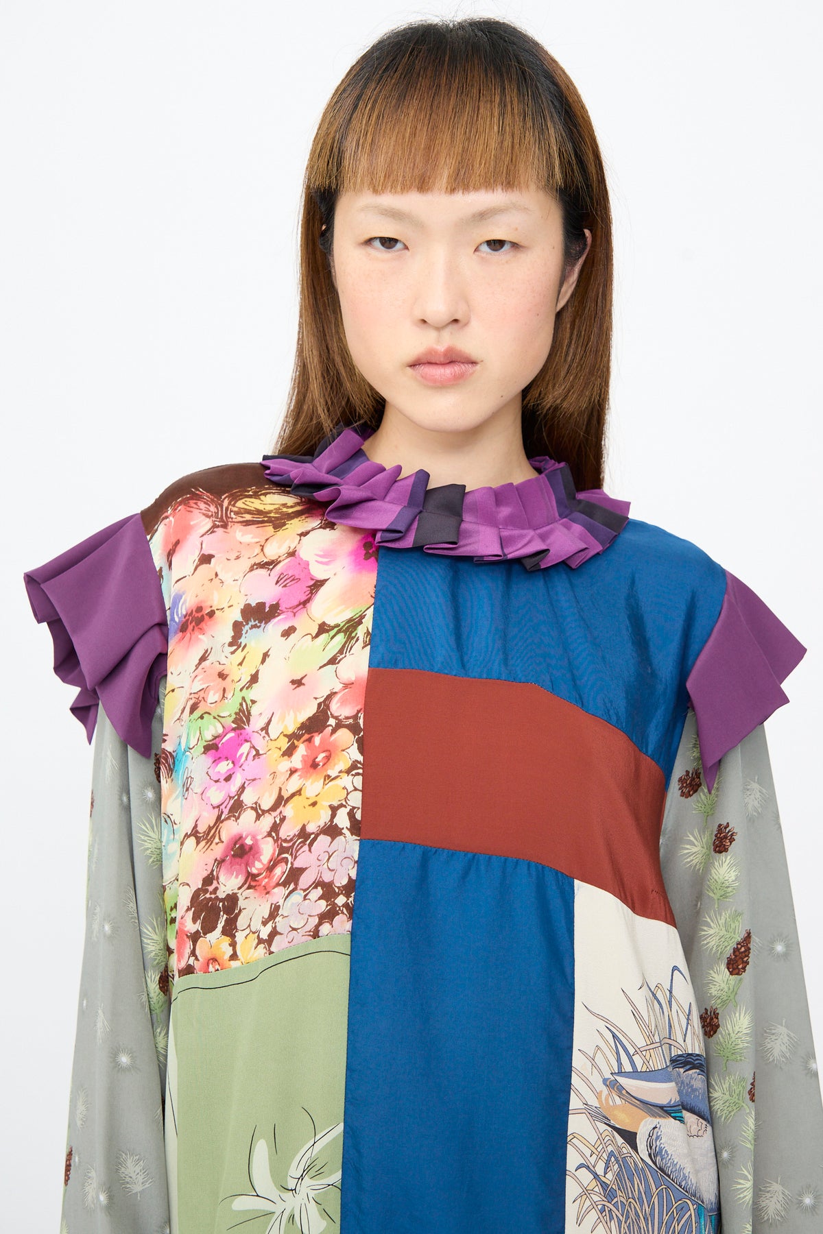 A person wears the Bettina Bakdal Ruffled Collar and Shoulder Dress in Ilse Fehli, a vintage silk piece with a purple ruffled collar, shoulder accents, and multicolored floral and pinecone panels.