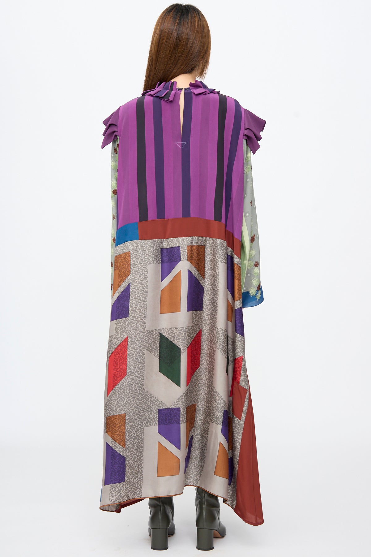 A person seen from behind wears the Bettina Bakdal Ruffled Collar and Shoulder Dress in Ilse Fehli, a sleeveless, calf-length silk style with a ruffled collar, purple stripes, and a geometric skirt.
