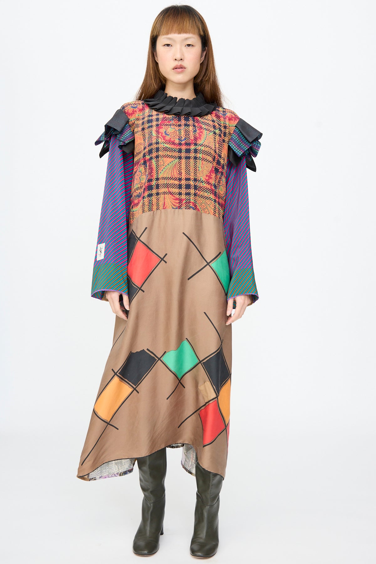 A model wears a Bettina Bakdal Ruffled Collar and Shoulder Dress in Marguerite Friedlaender, a long-sleeved silk dress featuring a black ruffled collar, shoulder ruffles, plaid bodice, and diamond skirt.