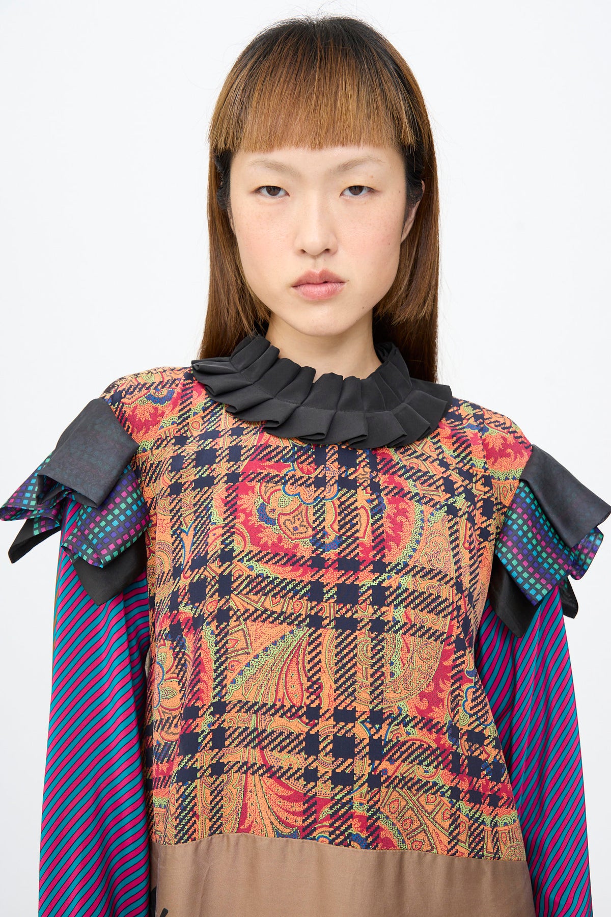 Model wearing a Bettina Bakdal Ruffled Collar and Shoulder Dress in Marguerite Friedlaender, featuring a patchwork design with a ruffled collar, cap sleeves, plaid, paisley, and stripes.
