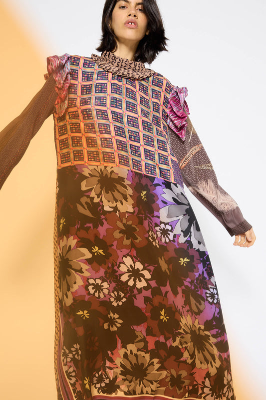 A person wearing the Bettina Bakdal Ruffled Collar and Shoulder Dress in Heather Blossom, which features floral and geometric designs, standing against a light background.