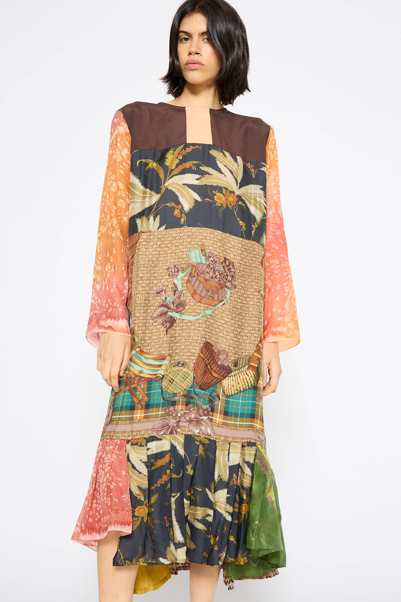 A person is wearing the Silk Hannah Dress in Forest Lunch by Bettina Bakdal, featuring a multicolored patchwork with long sleeves, a relaxed fit, various patterns, and floral designs. The dress is crafted from up-cycled vintage silk.