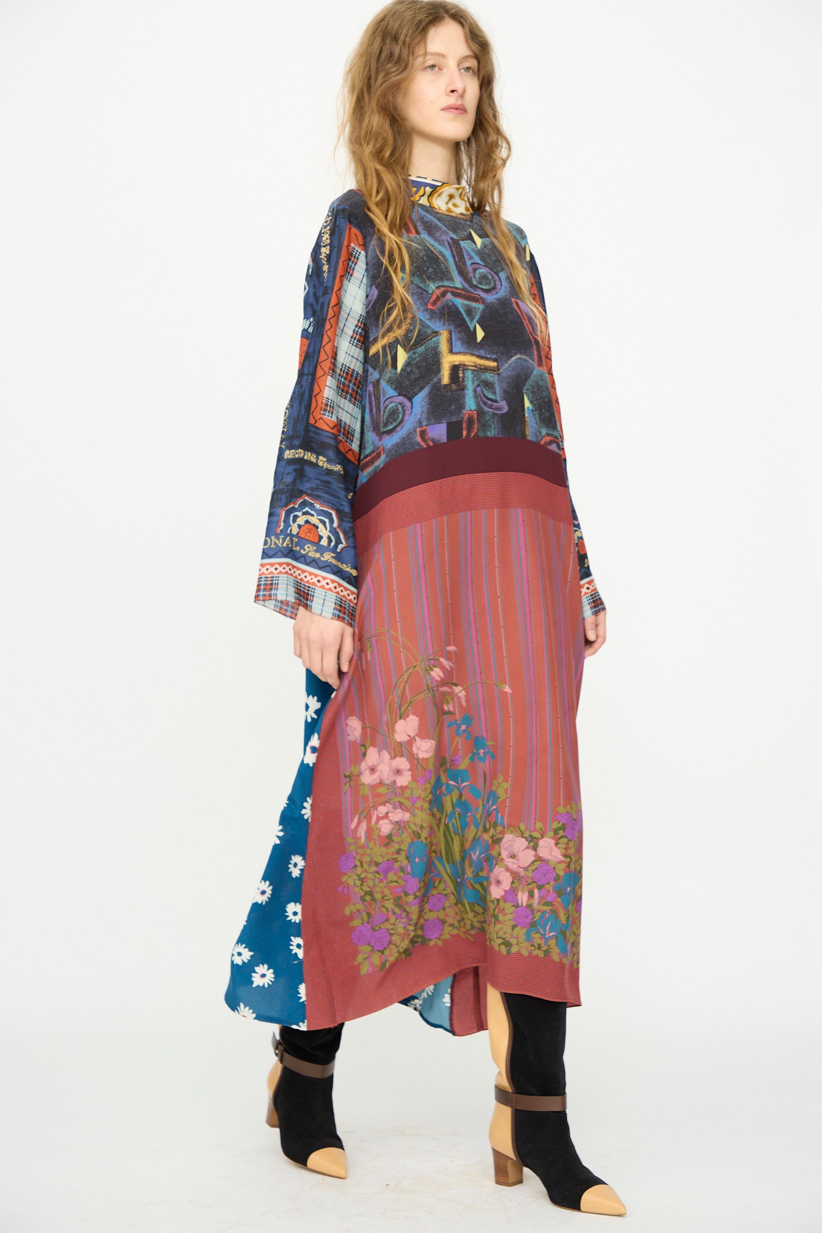 A woman stands against a white background wearing the Bettina Bakdal Classic Mandarin Collar Vintage Scarves Dress in Myriam Manuckiam, styled with black heeled boots.