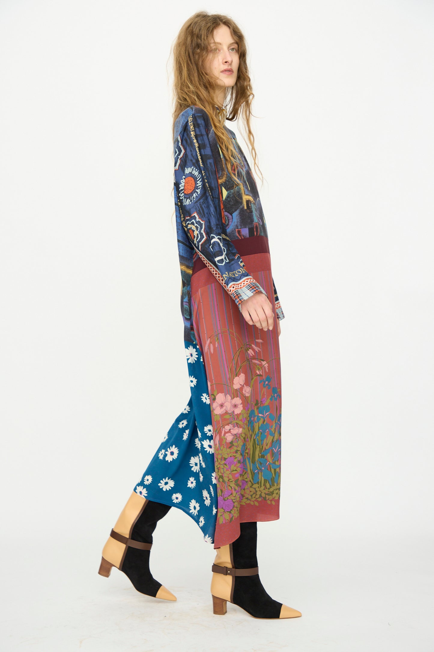 A woman in profile wears the Bettina Bakdal Classic Mandarin Collar Vintage Scarves Dress in Myriam Manuckiam, featuring a blue patterned top and floral multi-patterned skirt, paired with black tights and tan-heeled sandals against a white backdrop.