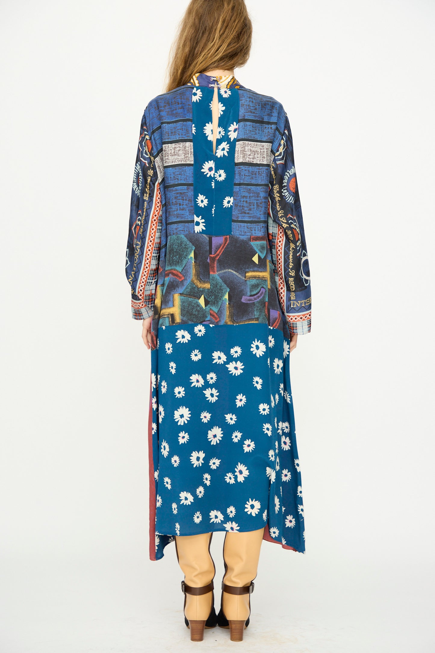 A person stands facing away, wearing the Bettina Bakdal Classic Mandarin Collar Vintage Scarves Dress in Myriam Manuckiam over beige pants and black heels.