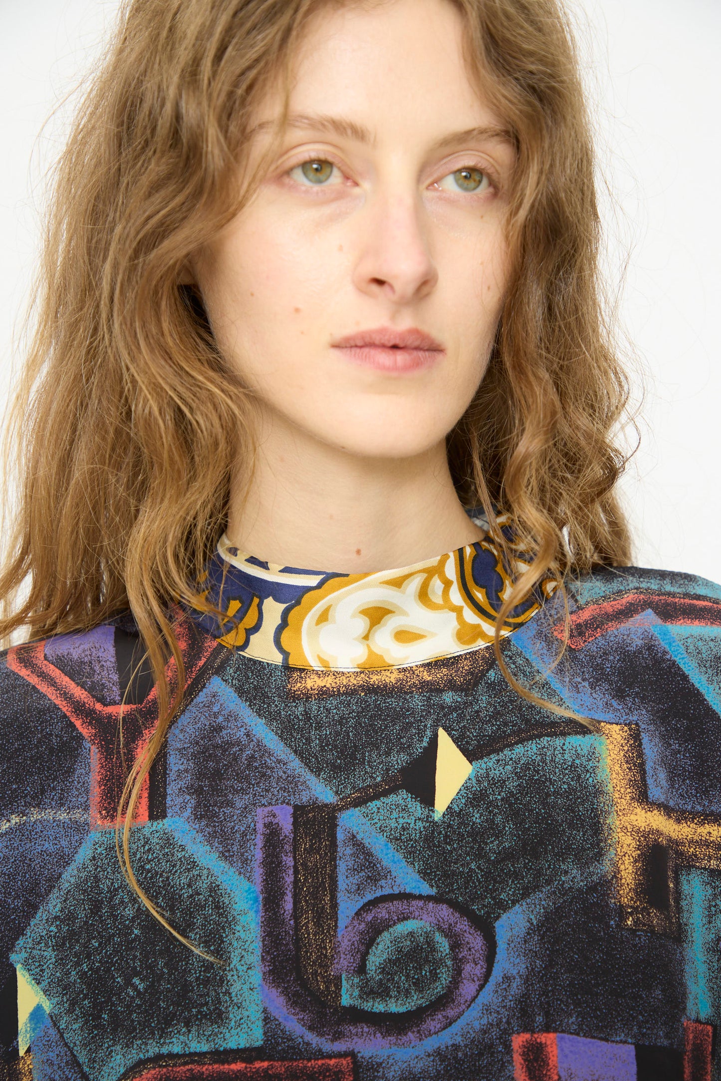 A person with long light brown hair wears the Bettina Bakdal Classic Mandarin Collar Vintage Scarves Dress in Myriam Manuckiam, featuring geometric patterns, and looks slightly to the side against a plain background.