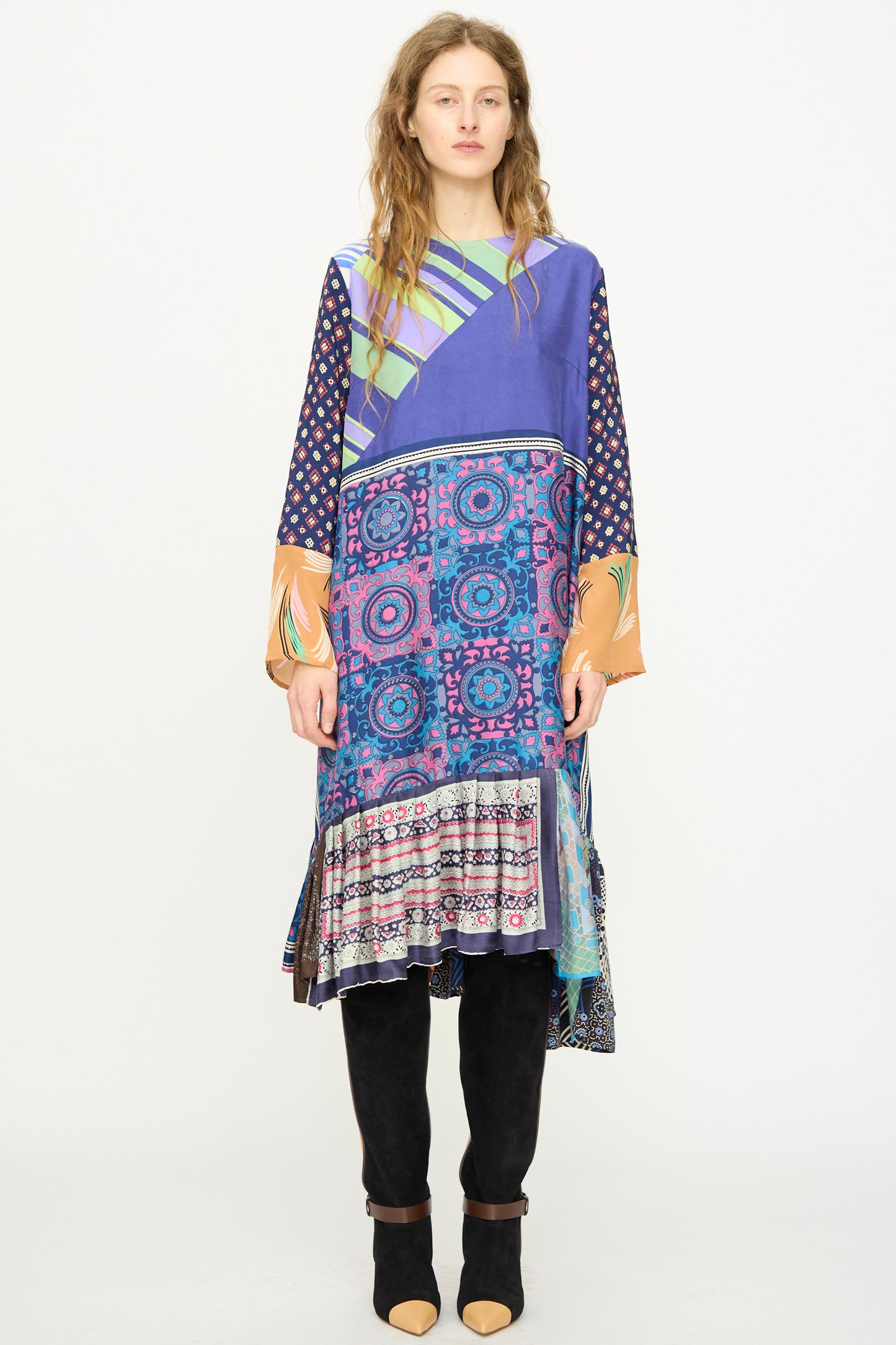 A woman faces forward wearing the Bettina Bakdal Hannah Silk Dress in Ricarda Meltzer, a colorful long-sleeved piece inspired by vintage silk scarves with geometric and floral patterns, styled with black knee-high boots.