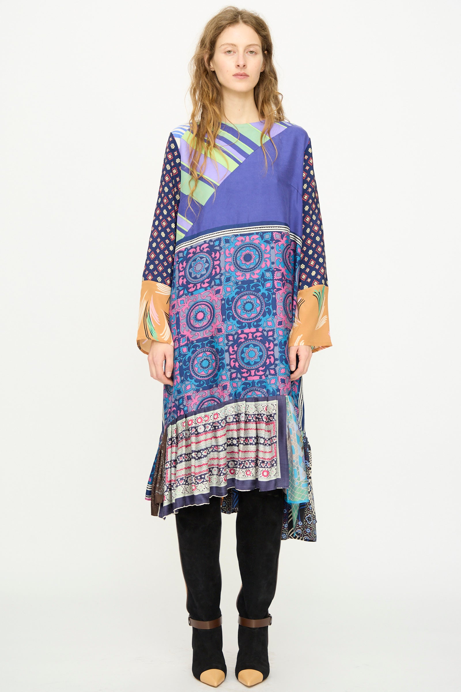 A woman faces forward wearing the Bettina Bakdal Hannah Silk Dress in Ricarda Meltzer, a colorful long-sleeved piece inspired by vintage silk scarves with geometric and floral patterns, styled with black knee-high boots.
