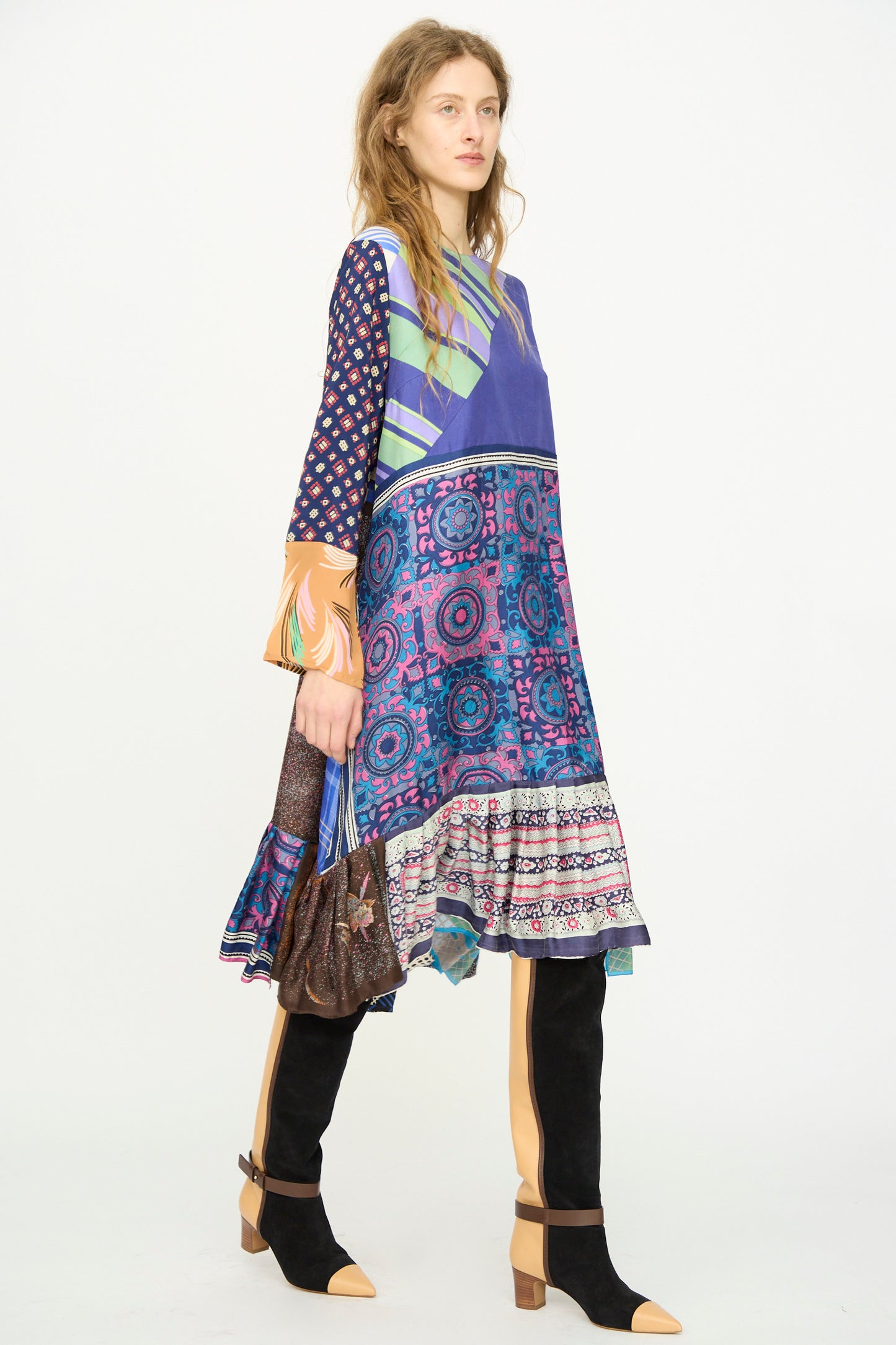 A woman wears the Bettina Bakdal Hannah Silk Dress in Ricarda Meltzer—crafted from colorful vintage silk scarves—with black and tan tall boots, standing against a plain white background.