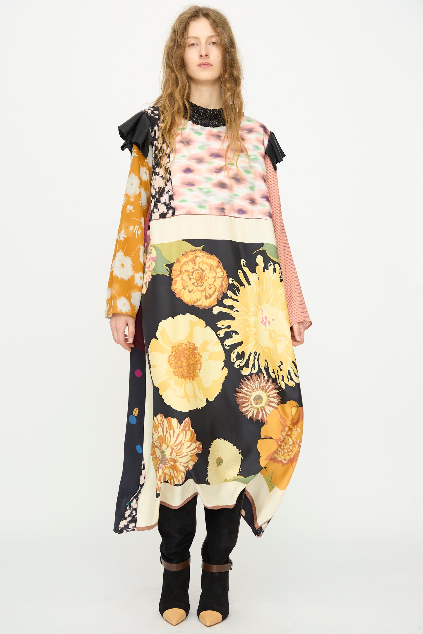 A person stands against a plain background wearing the Bettina Bakdal Ruffled Collar and Shoulder Vintage Scarves Dress in Edith Suschitzky, featuring mixed floral patterns and bold colors, paired with black boots.
