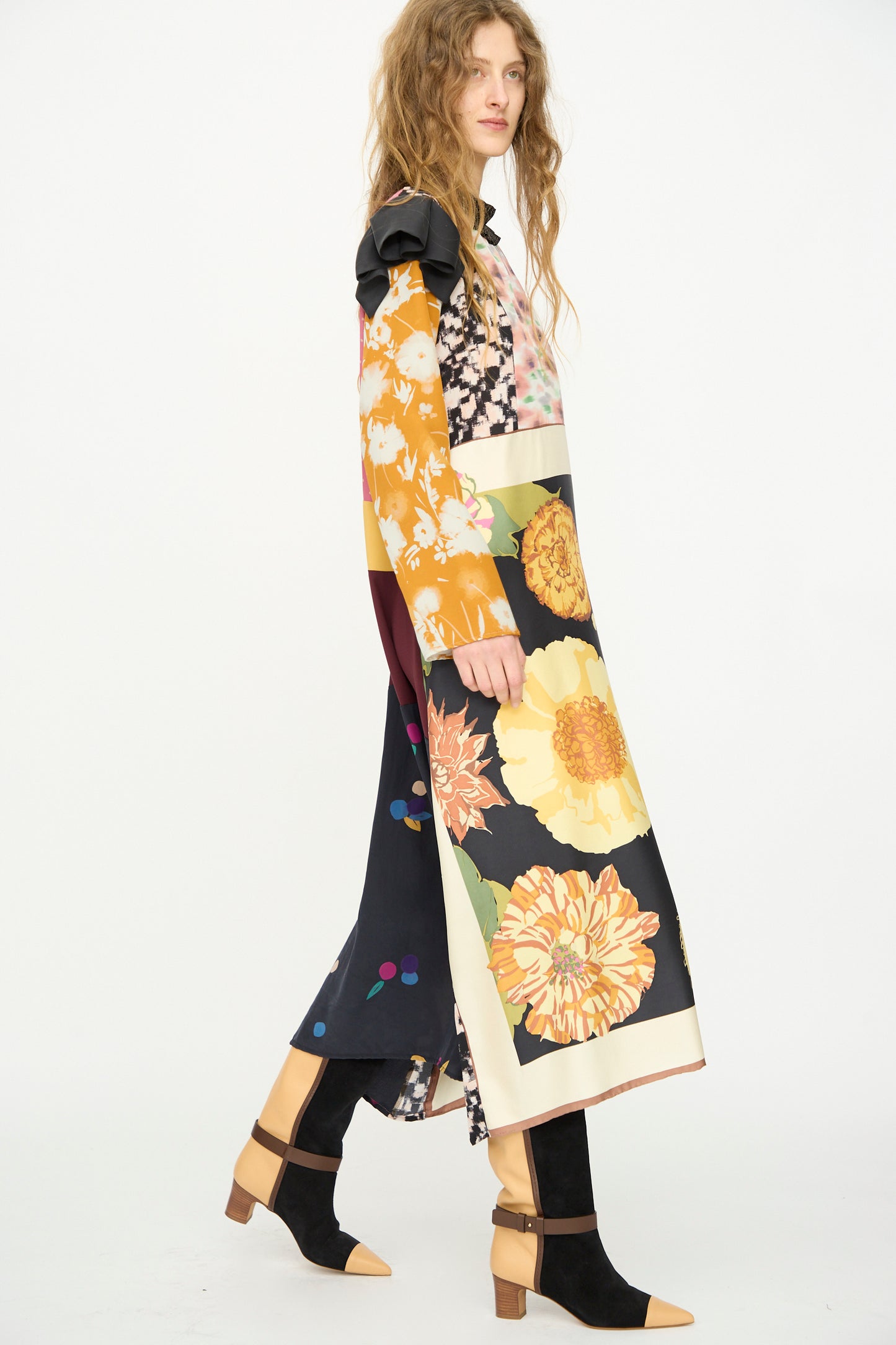 A woman with wavy hair wears the Bettina Bakdal Ruffled Collar and Shoulder Vintage Scarves Dress in Edith Suschitzky, paired with black tan-heeled shoes and black leggings, walking against a plain white background.