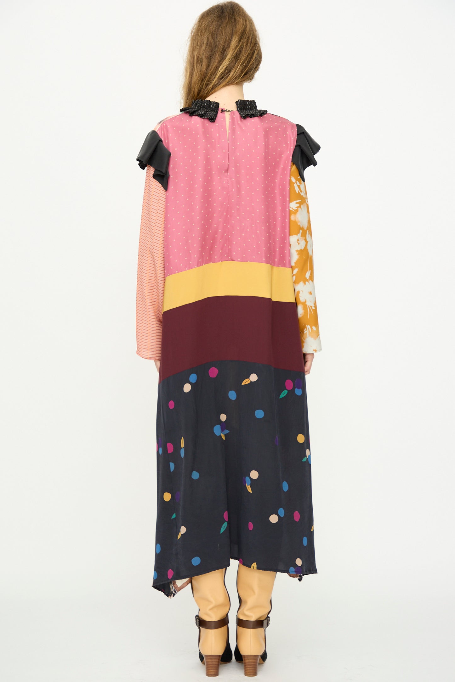 A person stands facing away, wearing the Bettina Bakdal Ruffled Collar and Shoulder Vintage Scarves Dress in Edith Suschitzky over tan pants and black shoes, set against a plain white background.