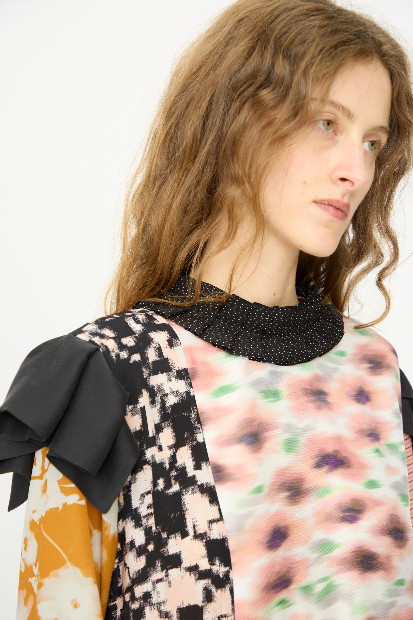 A person with long, wavy hair wears the Bettina Bakdal Ruffled Collar and Shoulder Vintage Scarves Dress in Edith Suschitzky, featuring up-cycled silk with mixed patterns and black ruffle details, looking slightly to the side.