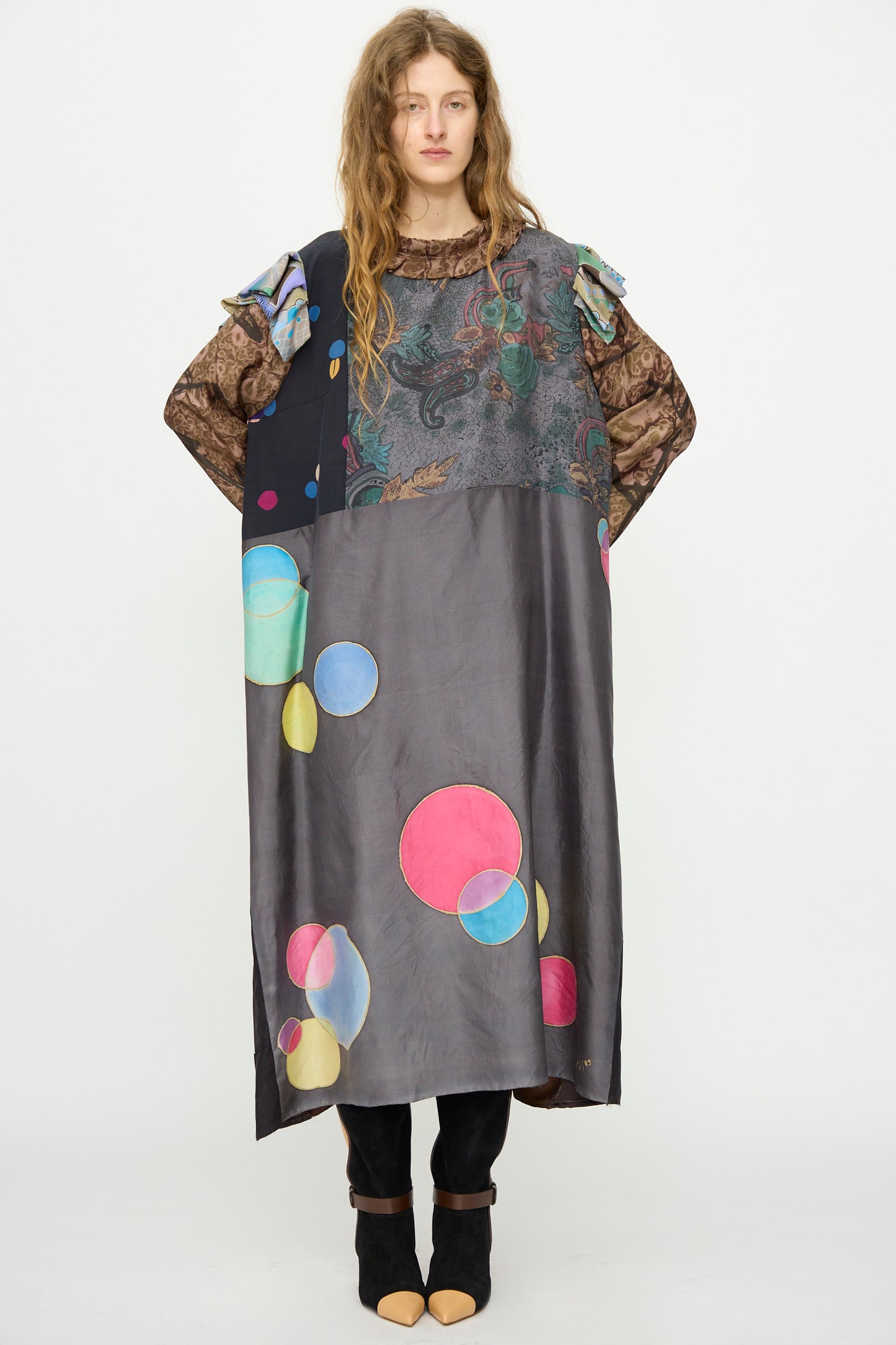 A woman faces forward in the Bettina Bakdal Ruffled Collar and Shoulder Vintage Scarves Dress in Margarete Dambeck, styled over black pants and open-toed shoes, set against a plain white background.