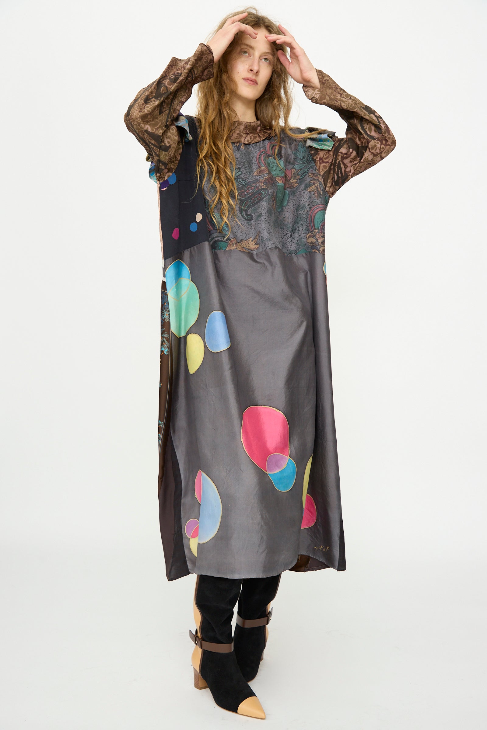 A person stands against a white background wearing the Bettina Bakdal Ruffled Collar and Shoulder Vintage Scarves Dress in Margarete Dambeck, styled with black pants and pointed black shoes.