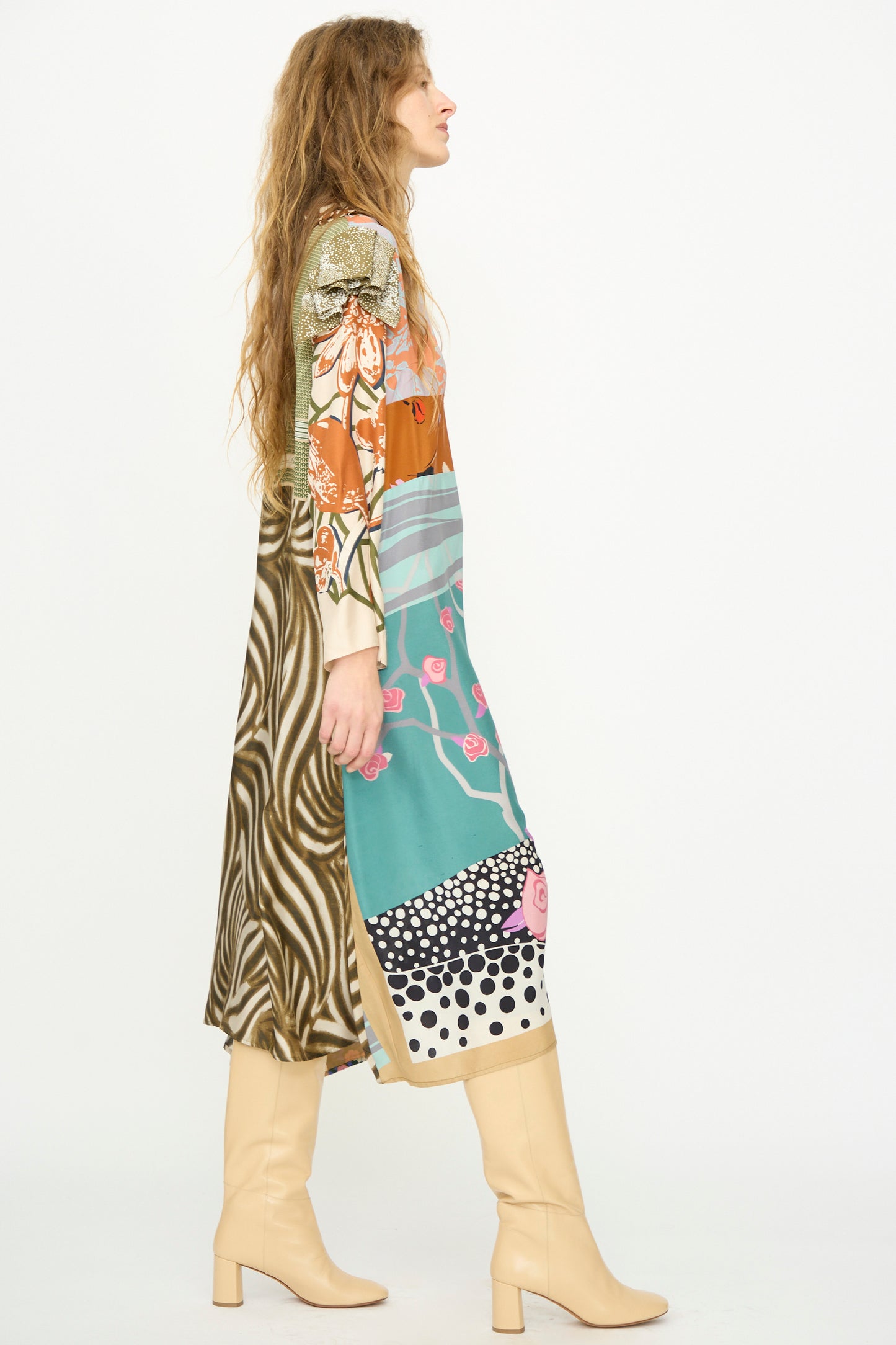 A woman in side profile wears Bettina Bakdal’s Ruffled Collar and Shoulder Vintage Scarves Dress in Dolores Del Bochum with beige knee-high boots, set against a plain white background.