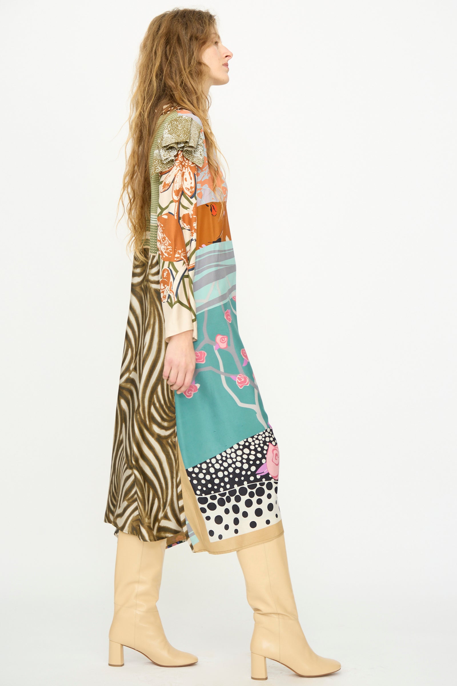 A woman in side profile wears Bettina Bakdal’s Ruffled Collar and Shoulder Vintage Scarves Dress in Dolores Del Bochum with beige knee-high boots, set against a plain white background.