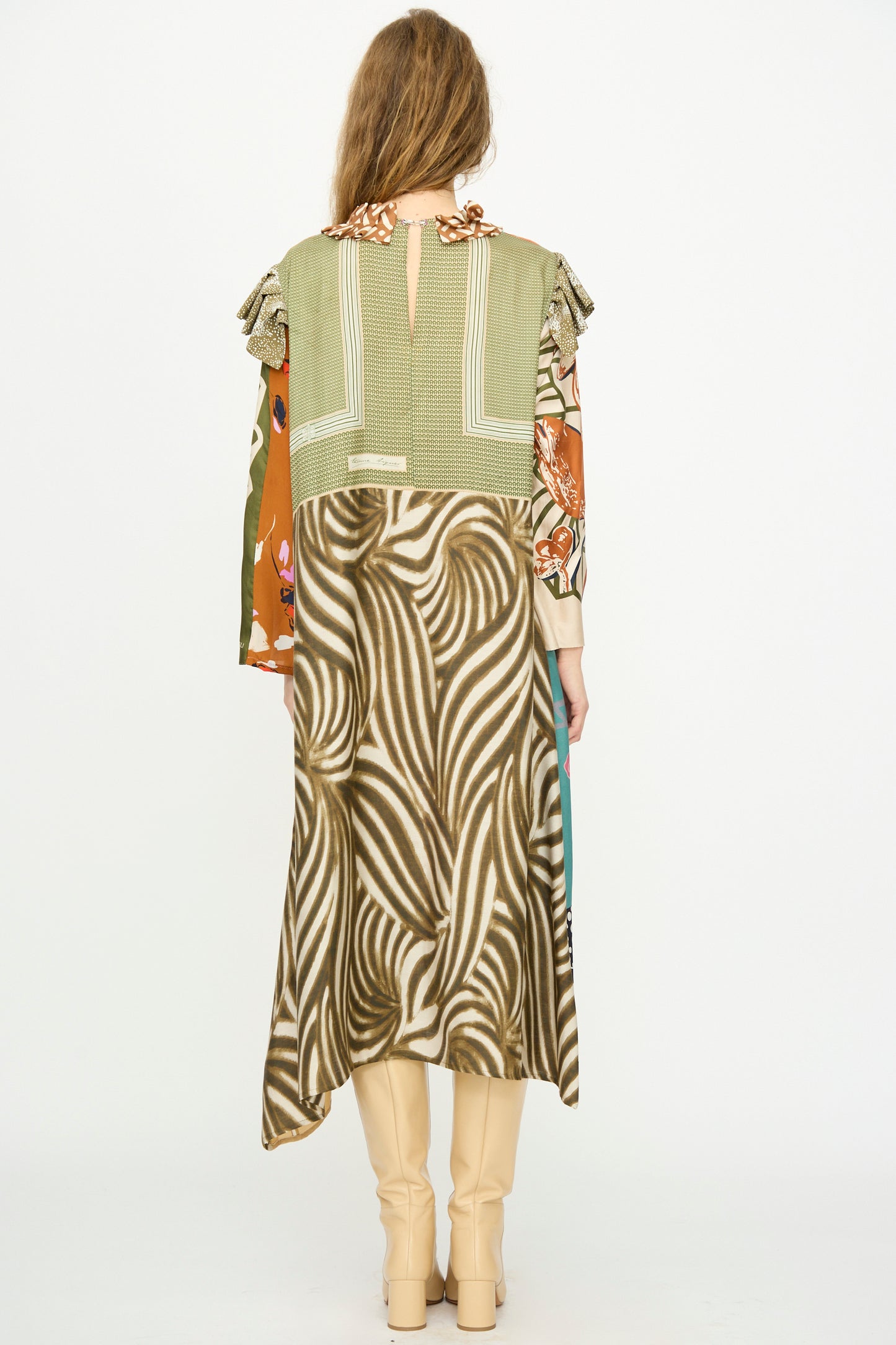 A person is shown from the back against a white background wearing Bettina Bakdal’s Ruffled Collar and Shoulder Vintage Scarves Dress in Dolores Del Bochum, featuring up-cycled silk in green, beige, and brown tones with long sleeves and cream knee-high boots.