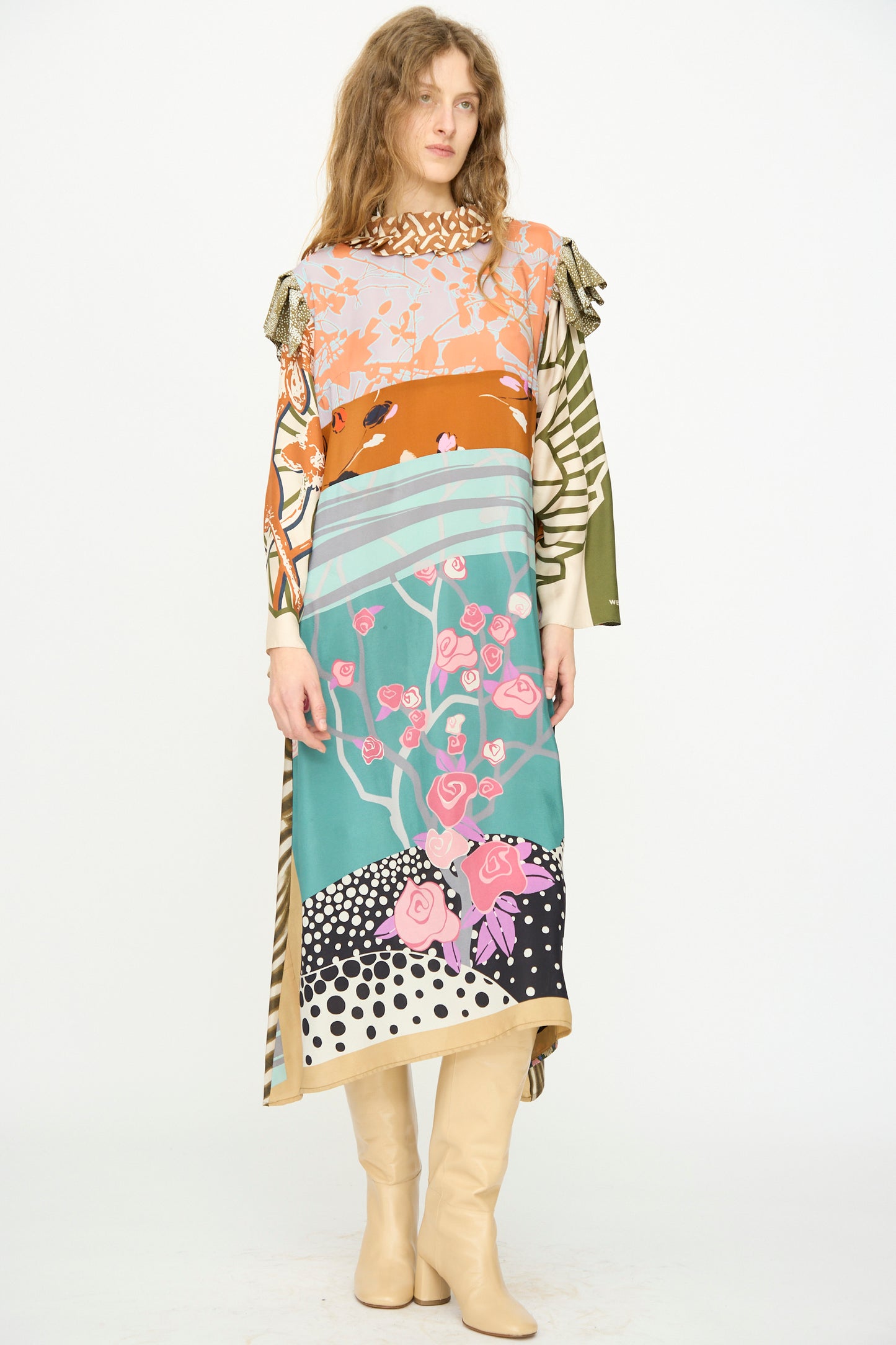 Model wears the Bettina Bakdal Ruffled Collar and Shoulder Vintage Scarves Dress in Dolores Del Bochum with beige boots, standing against a plain white background.