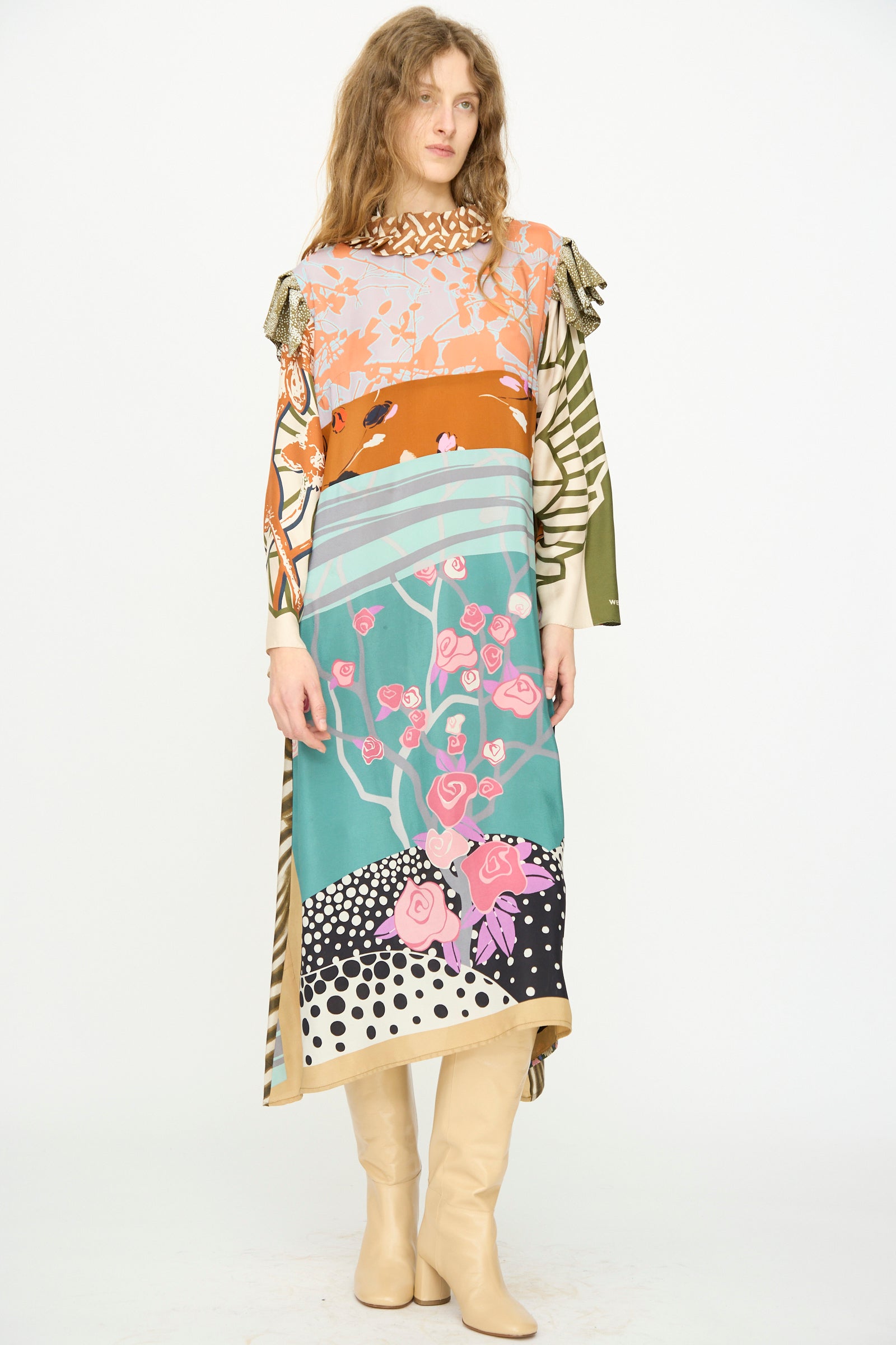 Model wears the Bettina Bakdal Ruffled Collar and Shoulder Vintage Scarves Dress in Dolores Del Bochum with beige boots, standing against a plain white background.