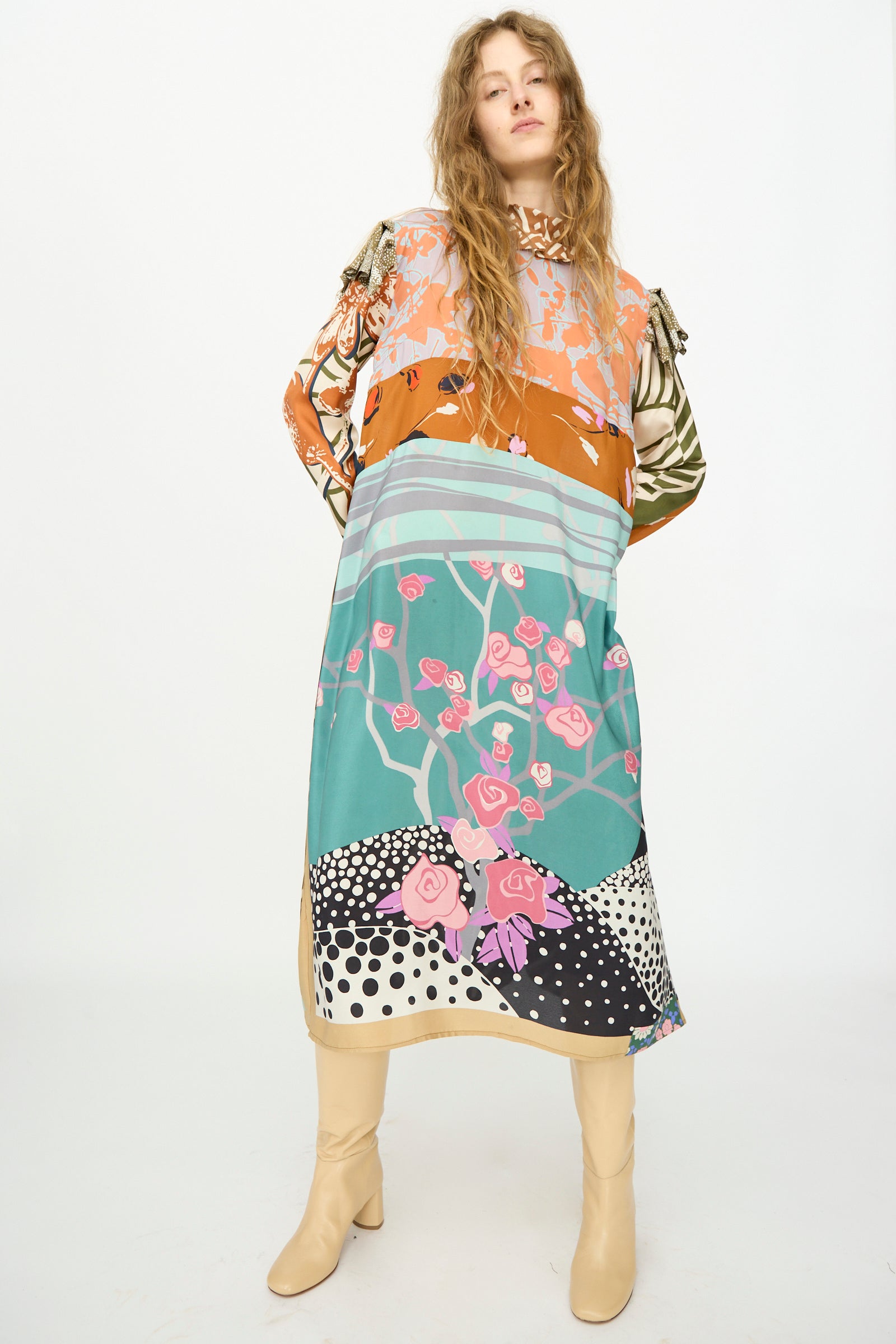 A woman wears the Bettina Bakdal Ruffled Collar and Shoulder Vintage Scarves Dress in Dolores Del Bochum, styled with cream knee-high boots, against a plain white background.