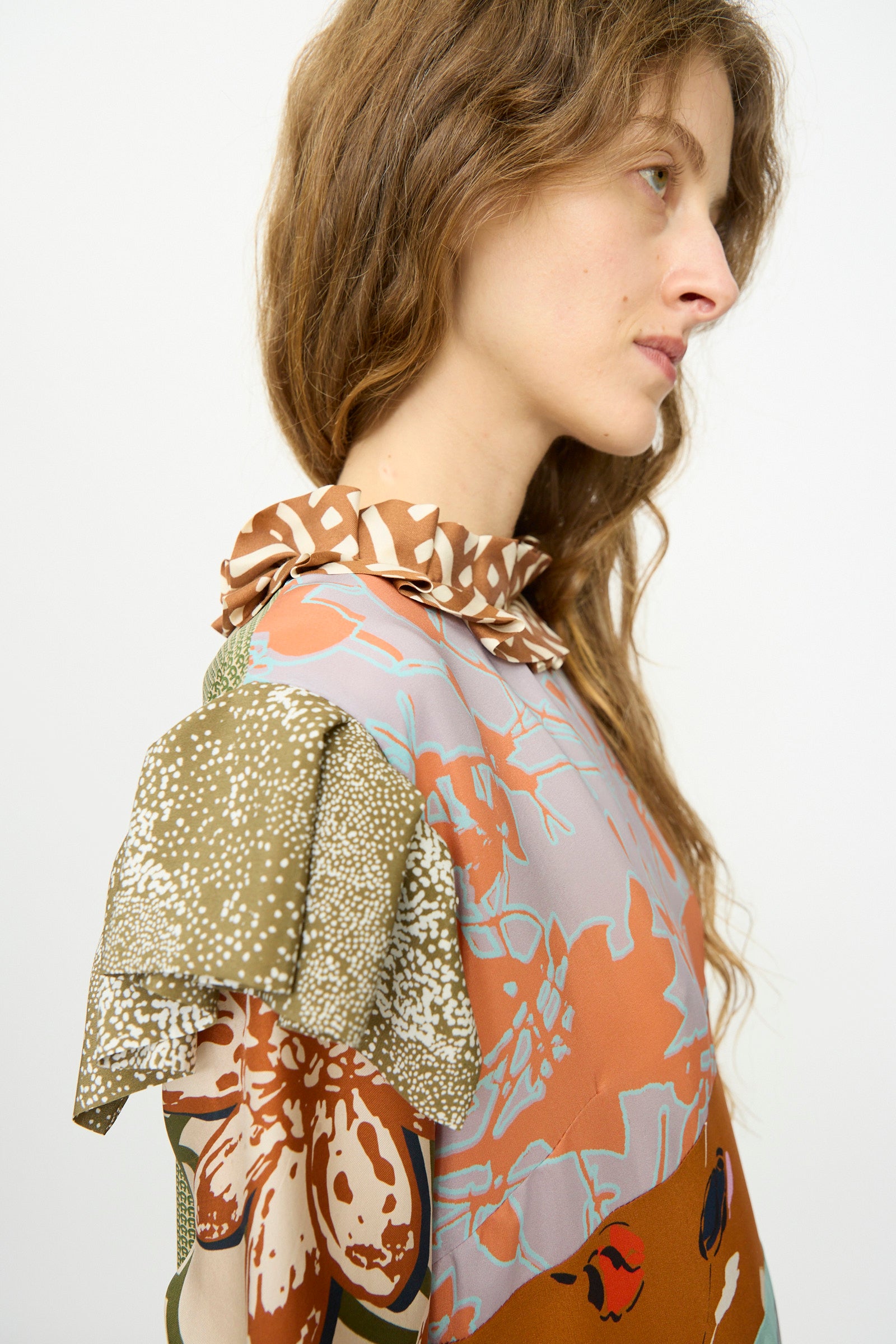 Woman with wavy light brown hair in profile wears the Bettina Bakdal Ruffled Collar and Shoulder Vintage Scarves Dress in Dolores Del Bochum, featuring a vibrant patchwork design, against a plain white background.