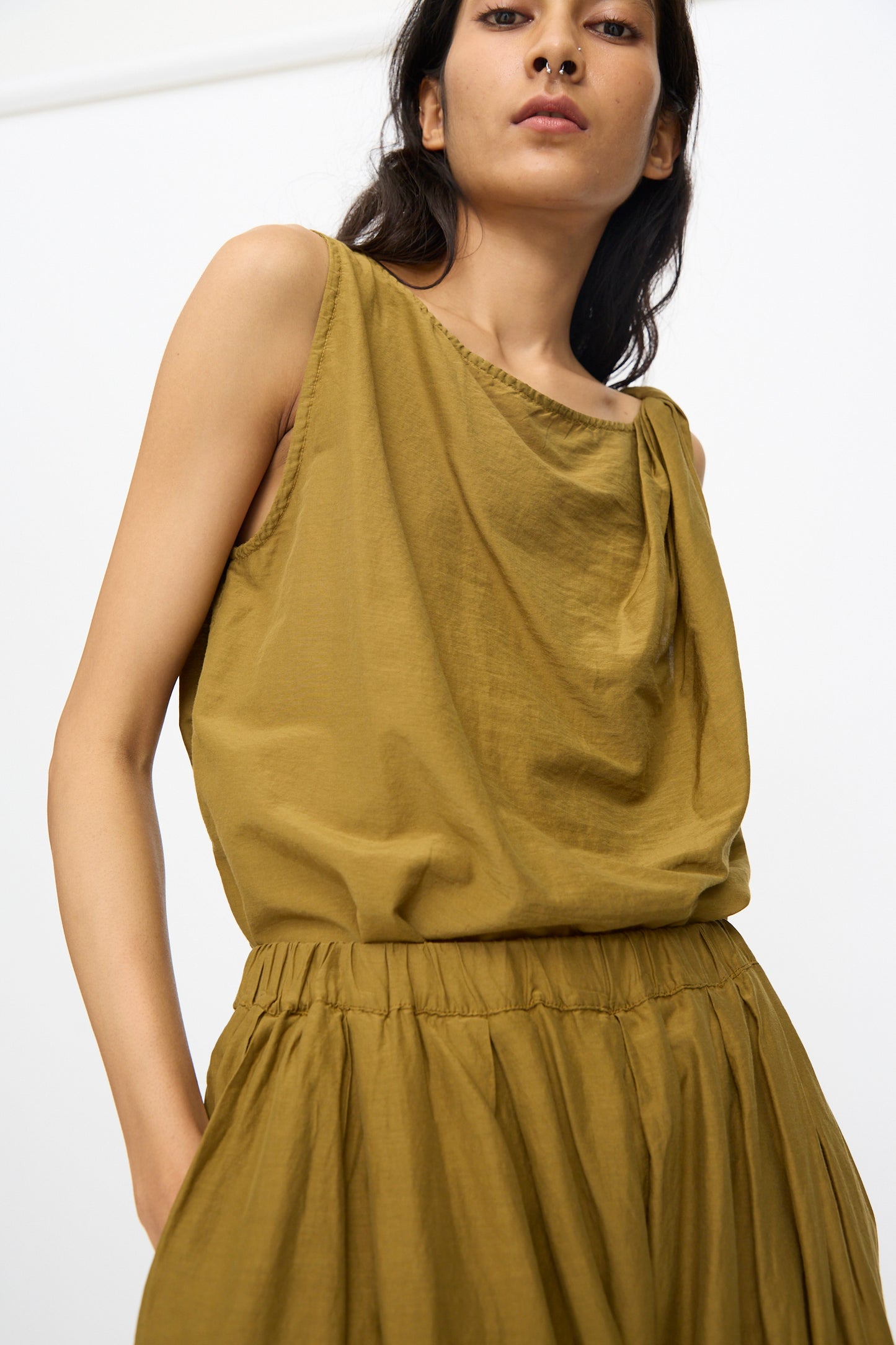 A woman wearing Black Crane's Akari Pants in Dark Olive stands against a plain white background.