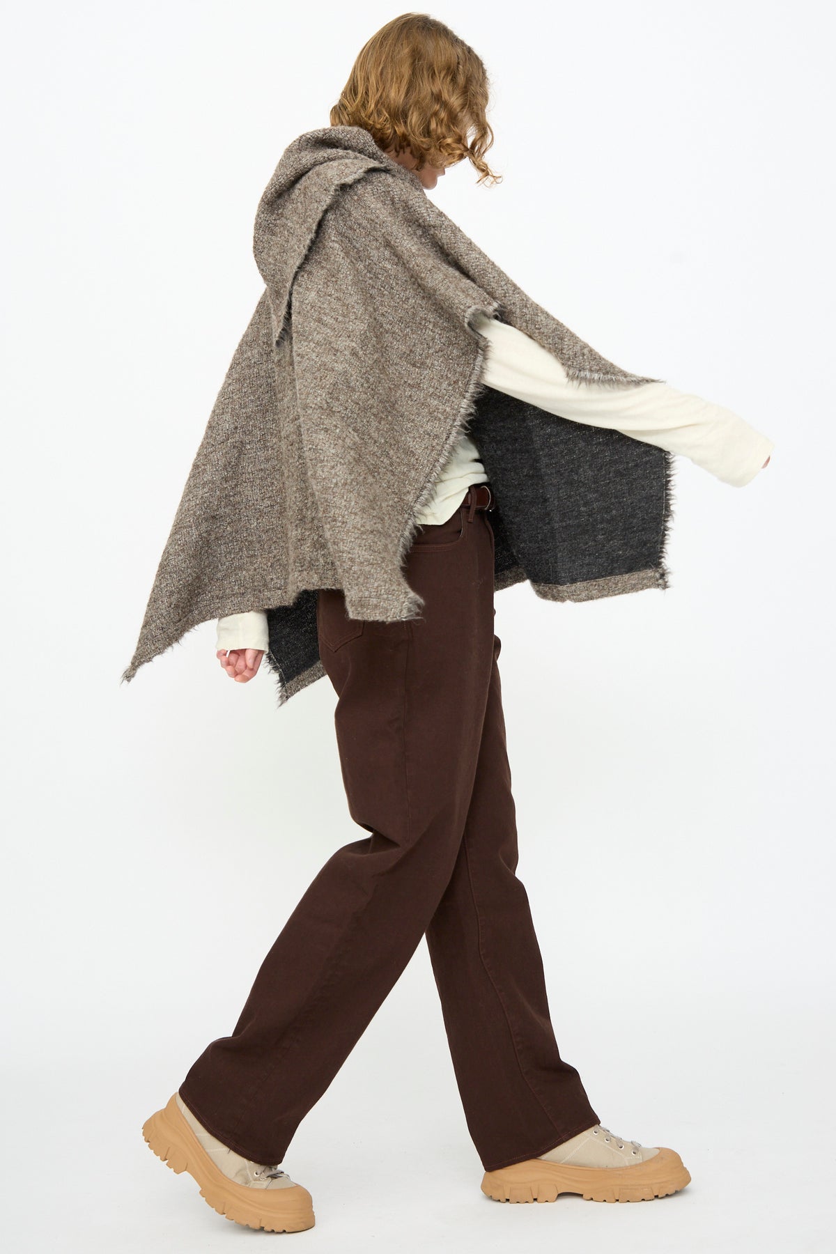 A person models the Black Crane Alpaca Short Poncho in Beige, paired with a cream long-sleeve shirt, brown pants, and tan shoes against a plain white background.