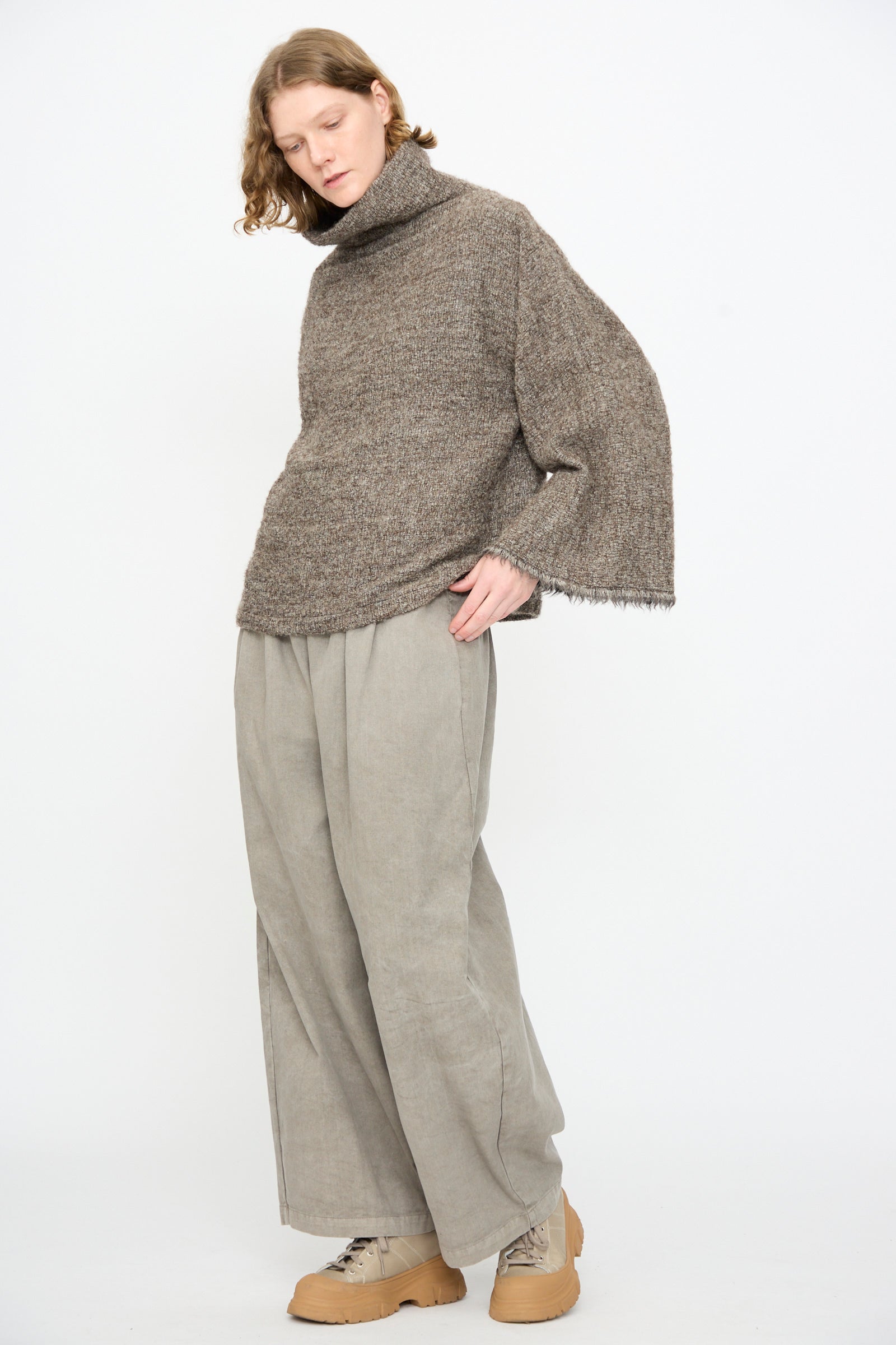A person standing against a plain background, wearing the Black Crane Alpaca Tube Top in Beige, wide beige pants, and tan platform shoes.