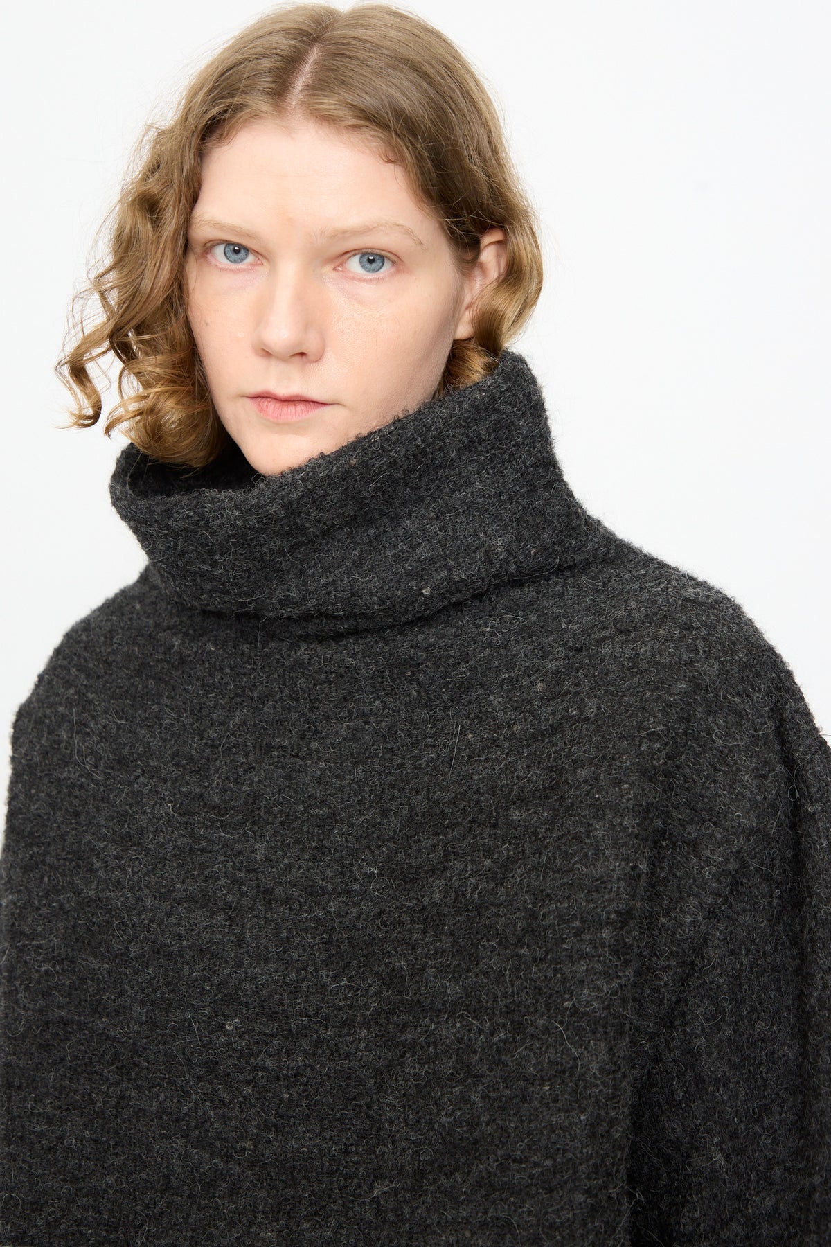 A person with shoulder-length wavy hair wears the Black Crane Alpaca Tube Top in Dark Grey, looking at the camera with a neutral expression against a plain background.