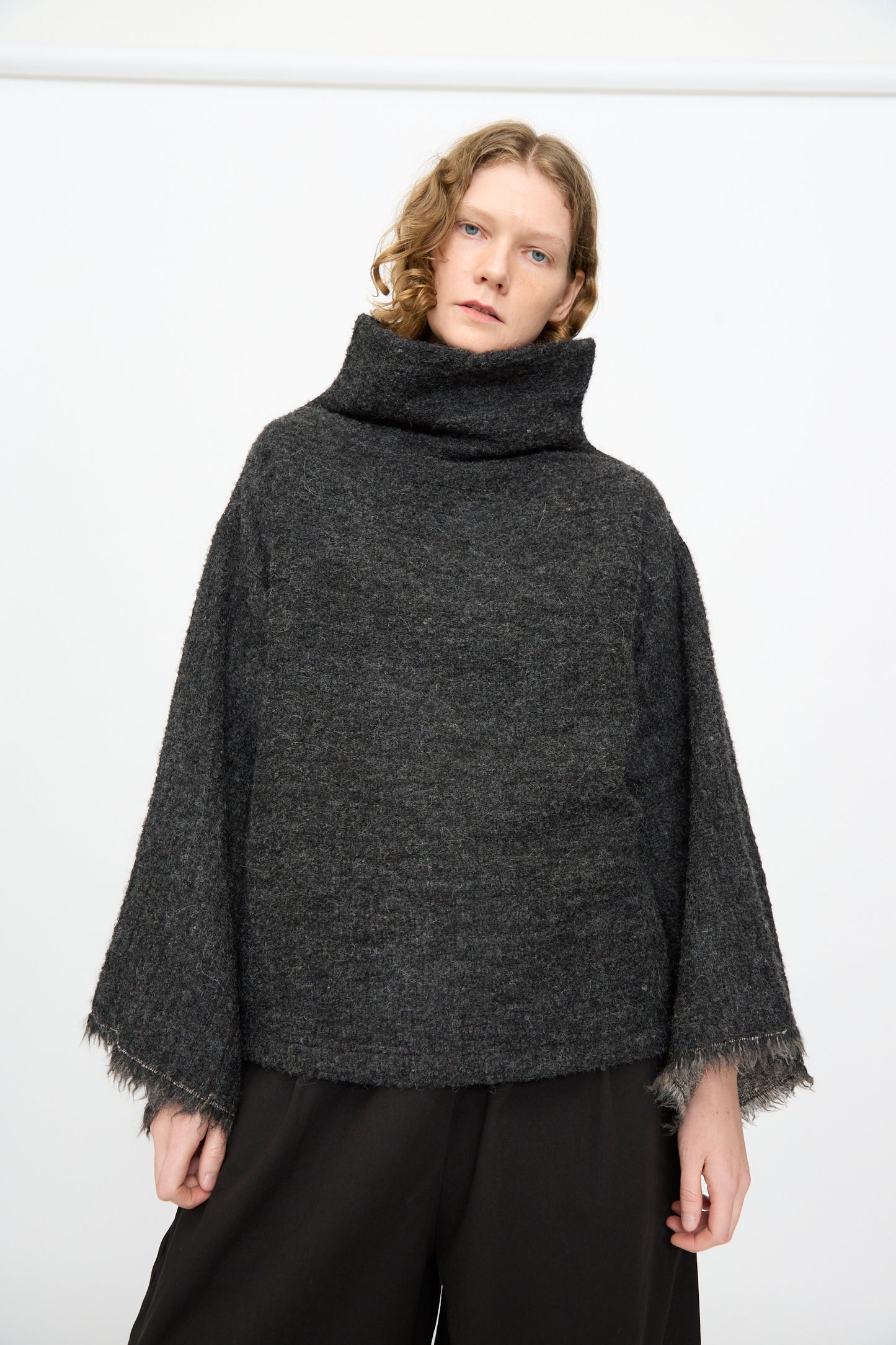 Wearing the Black Crane Alpaca Tube Top in Dark Grey, paired with black pants, a person stands against a plain white background.