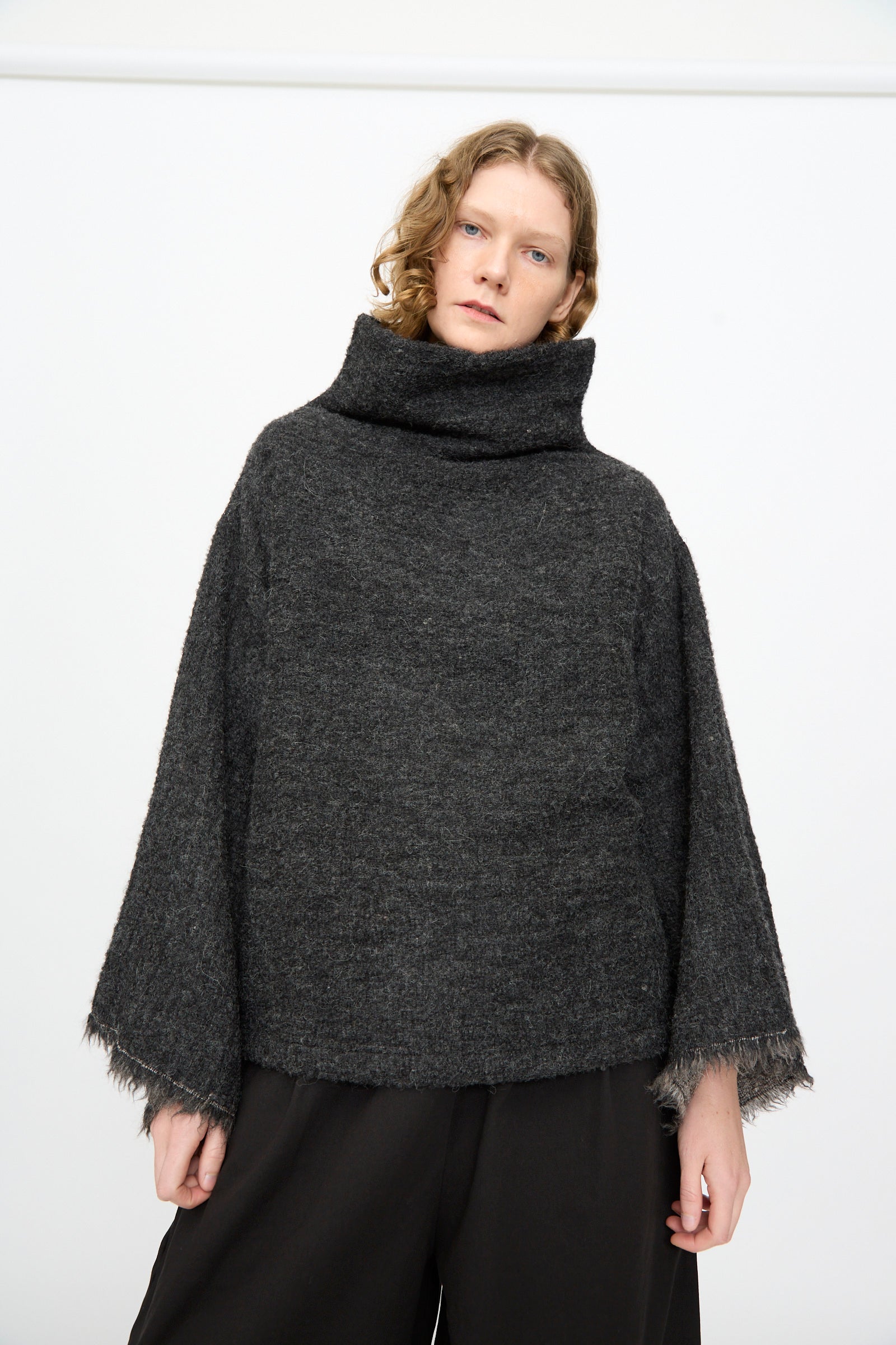 Wearing the Black Crane Alpaca Tube Top in Dark Grey, paired with black pants, a person stands against a plain white background.