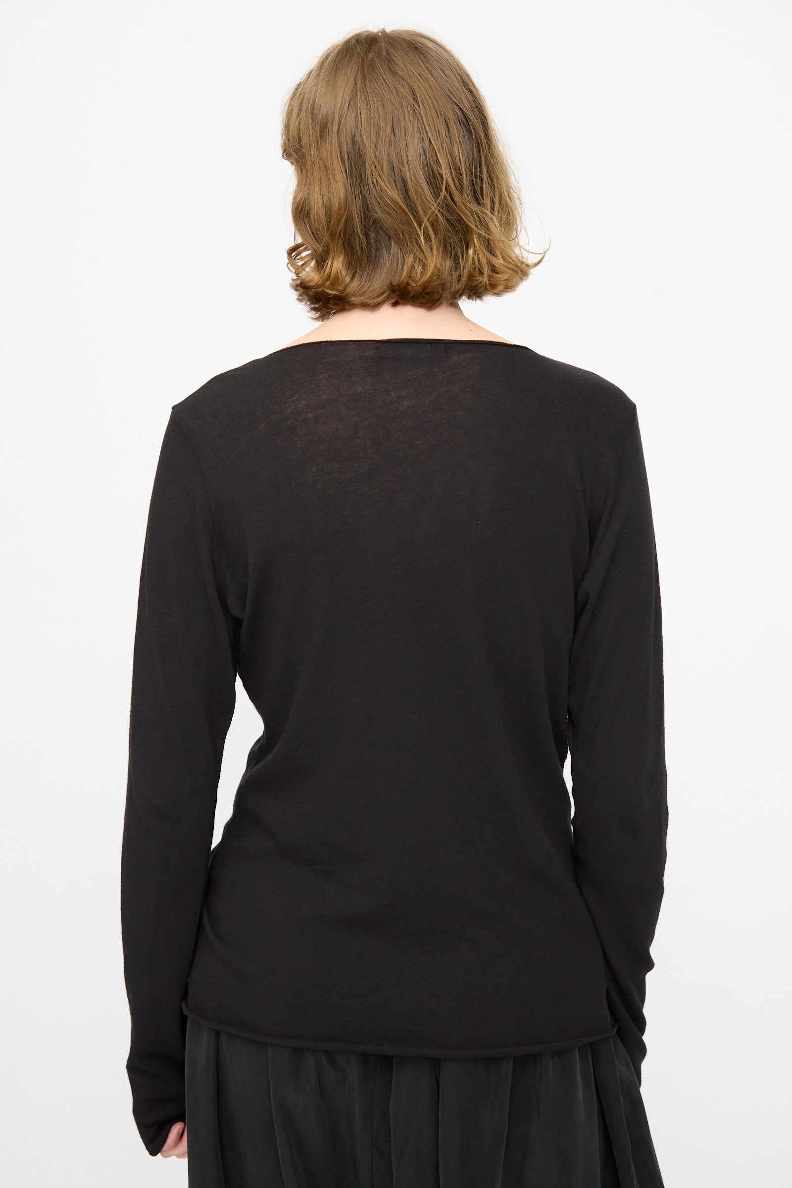 A person with short, light brown hair is shown from the back, wearing the Black Crane Boat Neck in Black—a relaxed fit long sleeve top—paired with a dark skirt, set against a plain white background.
