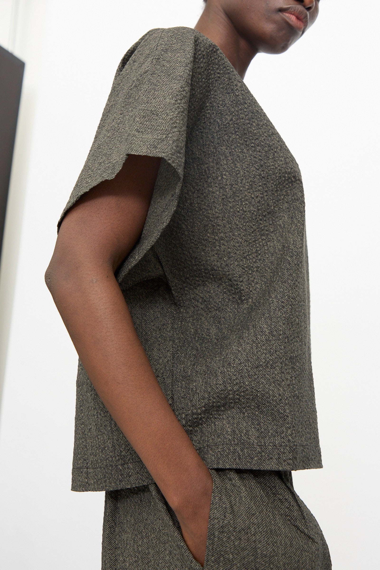 A person wearing the Black Crane Box Top with Micro Wave Texture in Steel, styled with matching pants and one hand in a pocket, stands against a plain background.