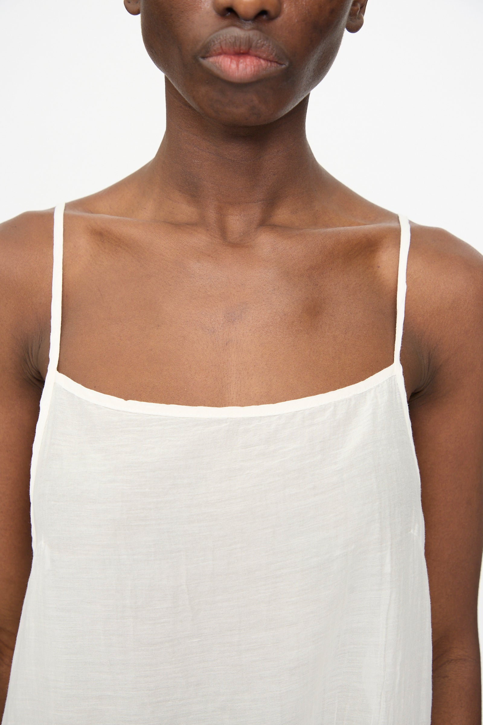Model wears the Black Crane Cami Dress in White, featuring spaghetti straps, photographed from shoulders to just above the lips against a plain background.