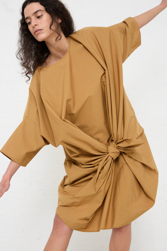 Woman in a relaxed fit, Organic Cotton Bow Dress in Camel by Black Crane posing with one arm outstretched.