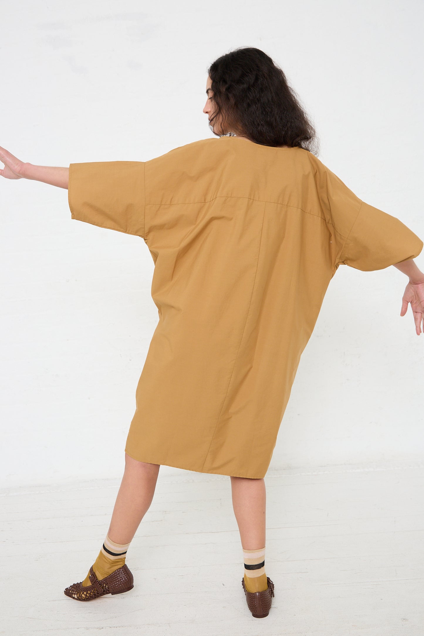 Woman in a Organic Cotton Bow Dress in Camel by Black Crane posing with arms outstretched.