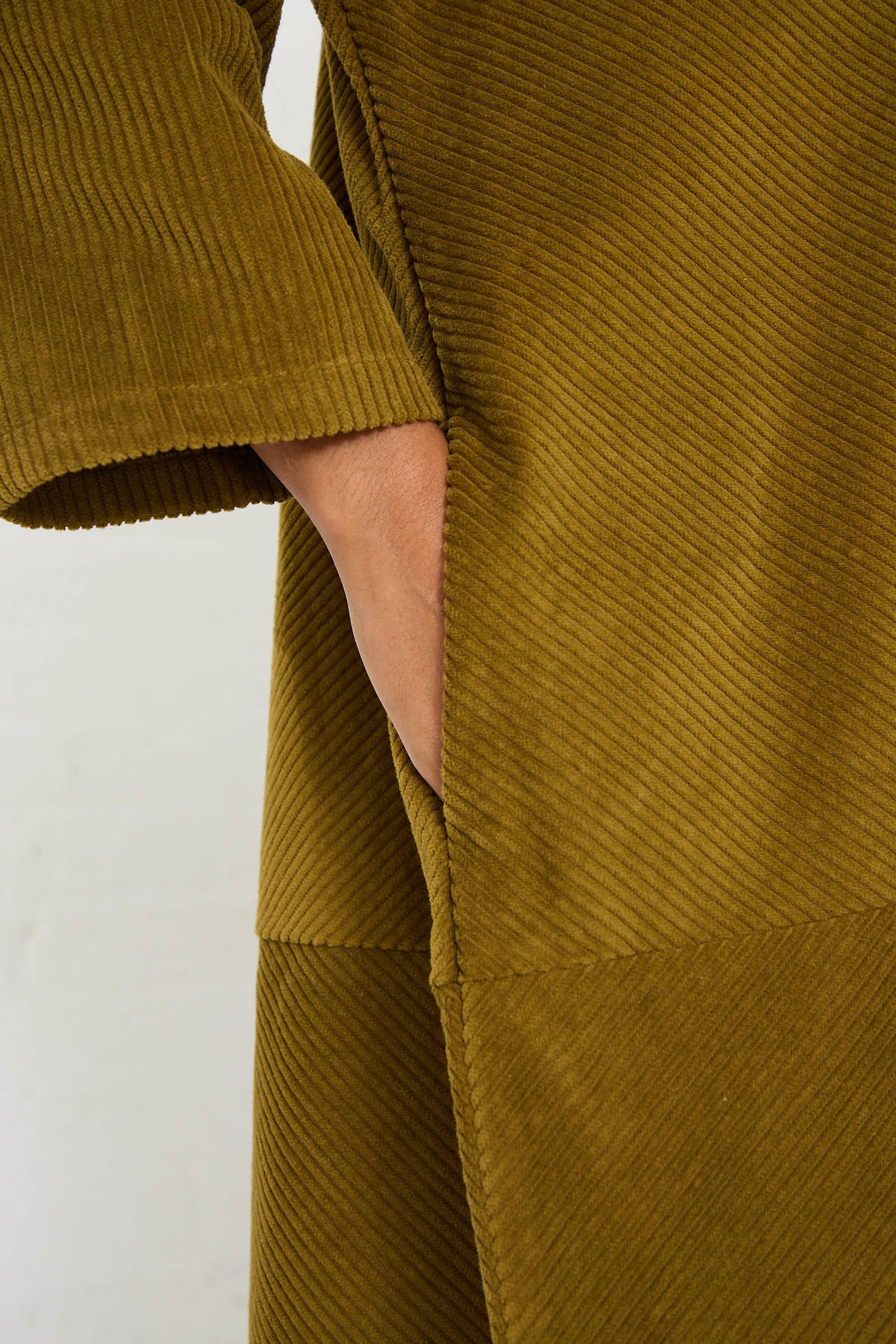 Close-up of a person’s hand in the pocket of a dark olive cotton corduroy garment. The fabric features a diagonal ribbed texture, giving the long sleeve midi dress by Black Crane an elegant touch.