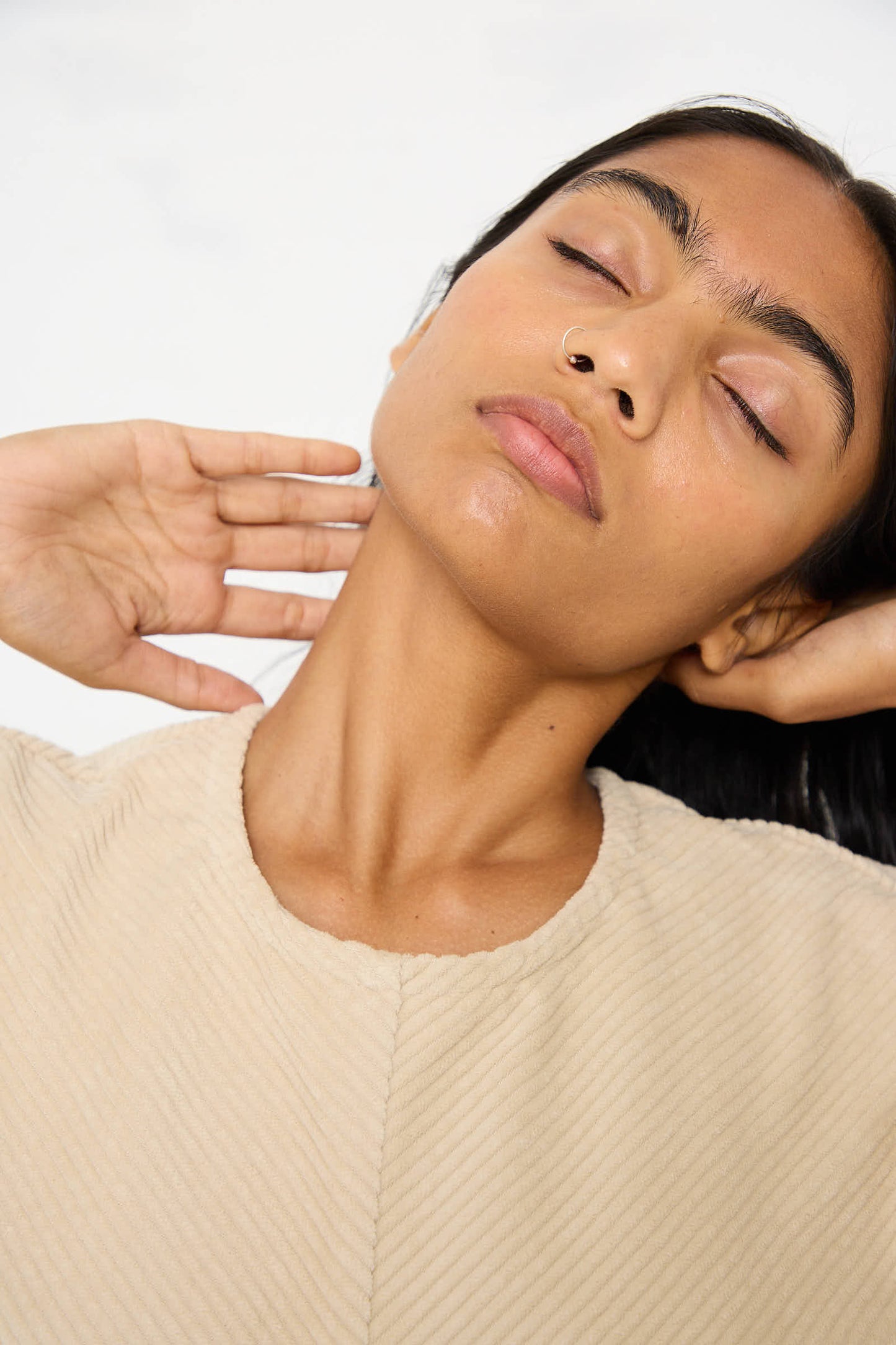 Person with eyes closed and hands behind the neck, wears the Cotton Corduroy Radient Dress in Ivory by Black Crane.