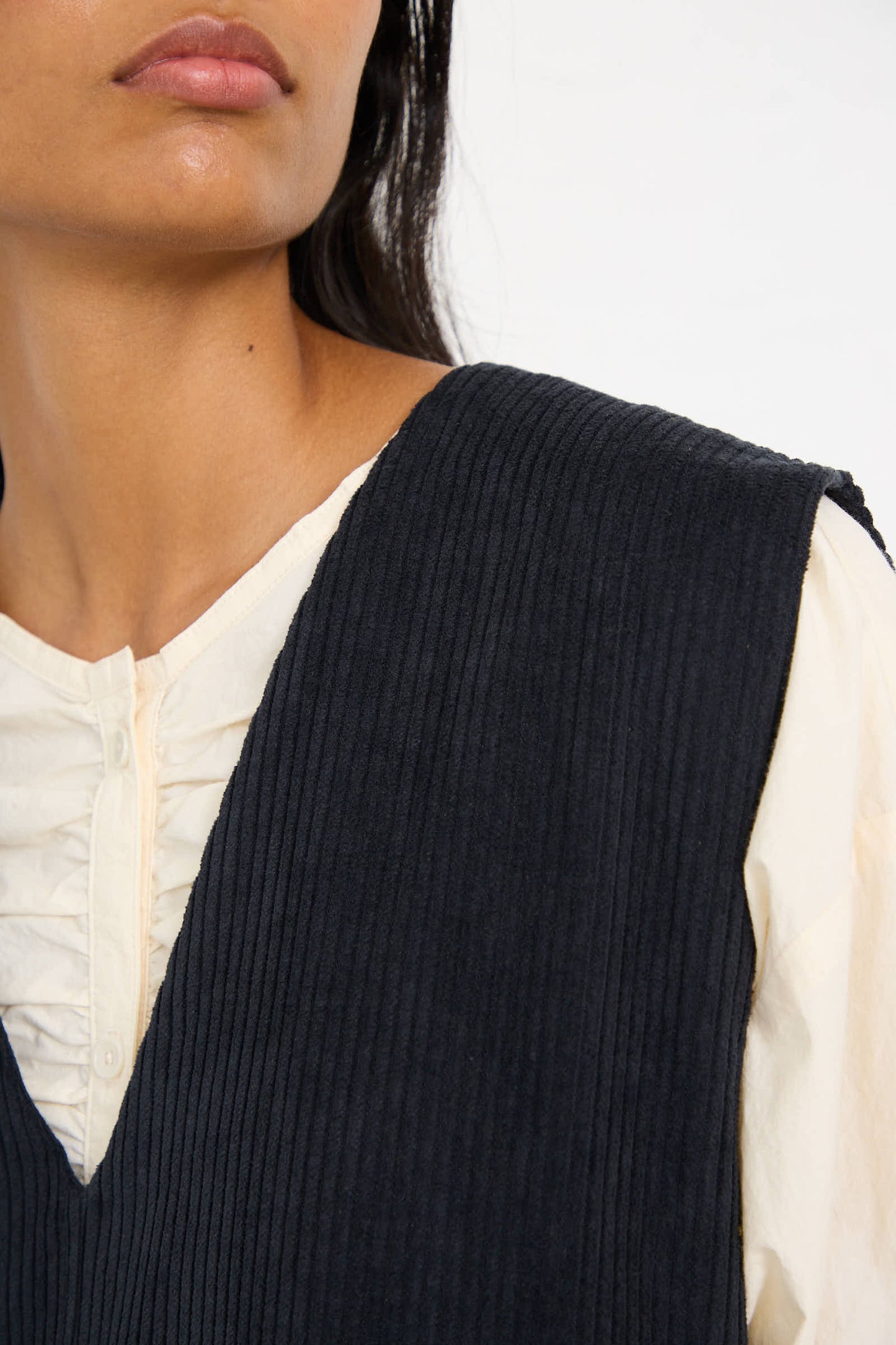 A person wearing a cream blouse and a relaxed-fit, black pinstriped dress, featuring the Cotton Corduroy Vest in Dark Grey by Black Crane, showing the upper part of their body.