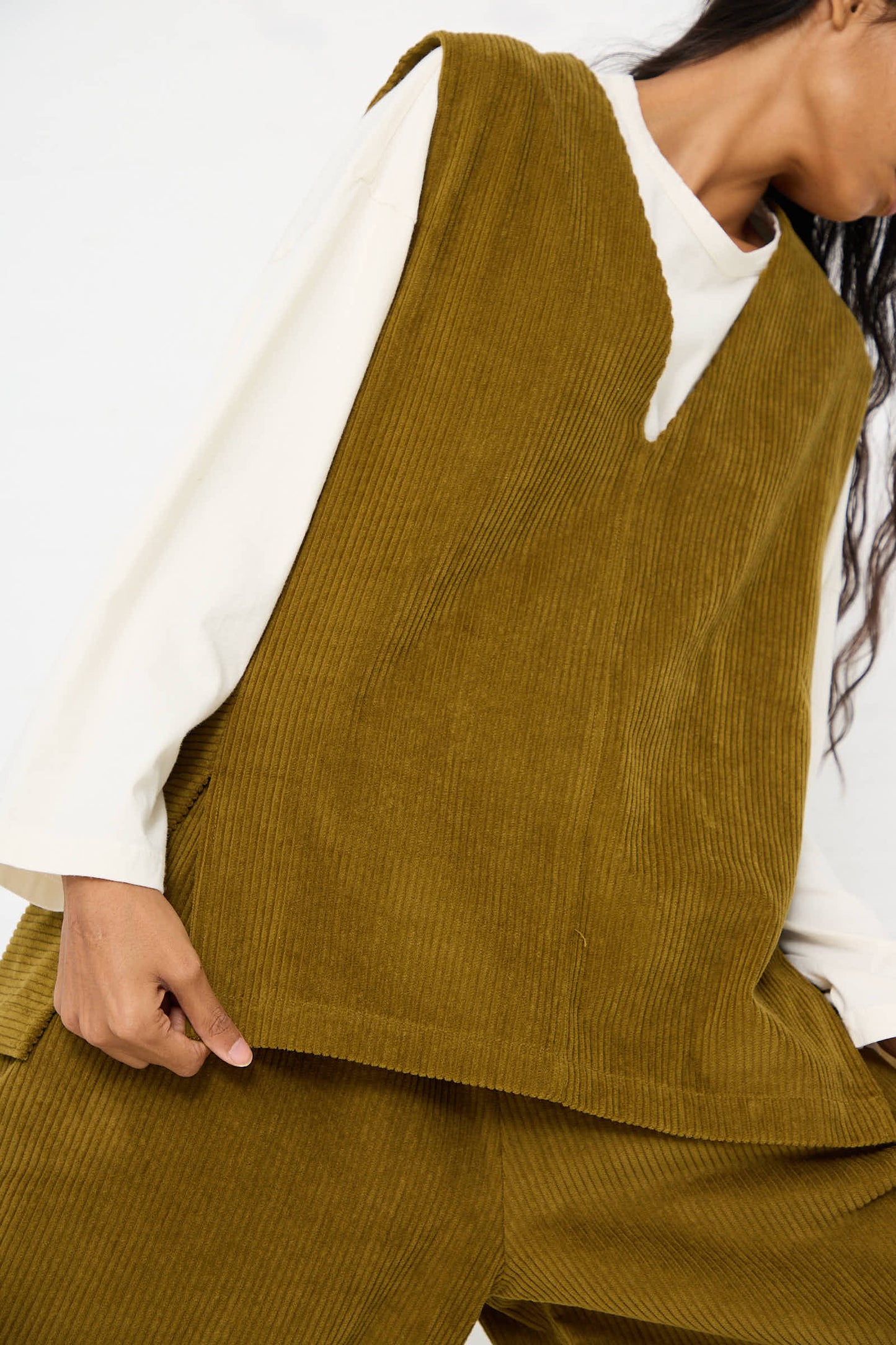 Person wearing a Black Crane Cotton Corduroy Vest in Dark Olive over a white long-sleeve shirt, with matching corduroy pants.