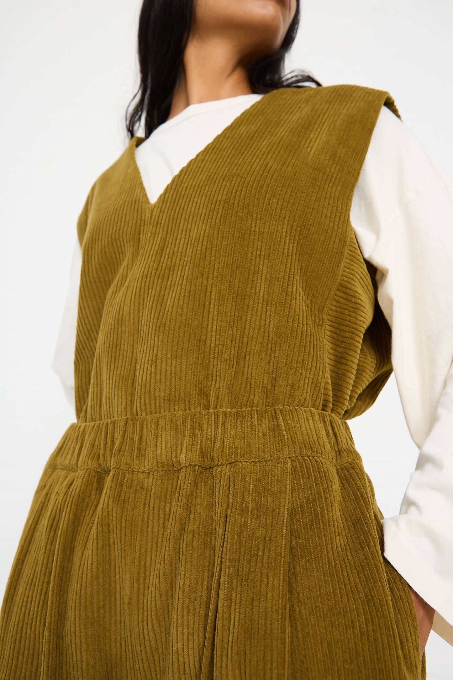 Person wearing a dark olive Cotton Corduroy Wide Pant by Black Crane with an elasticated waist over a white long-sleeve shirt, showcasing the pant's rich texture and comfortable design.