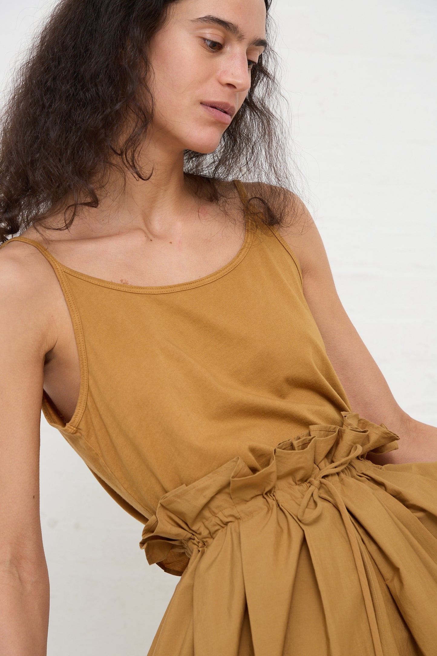 A woman in a Cotton Jersey Camisole in Camel by Black Crane holding a gathered piece of matching fabric.
