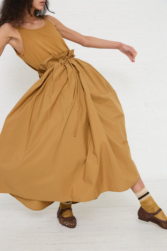 A person in a flowing Black Crane cotton parachute skirt in camel with a bow at the waist, mid-twirl, showcasing the dress's dynamics, paired with patterned brown shoes and striped socks.