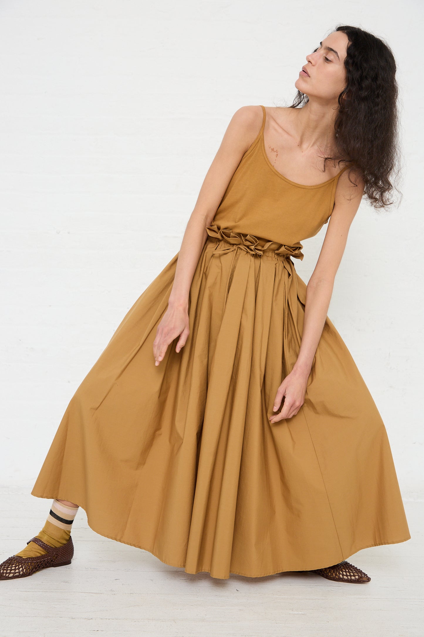 A woman in a Cotton Parachute Skirt in Camel by Black Crane featuring a braided belt poses against a white background.