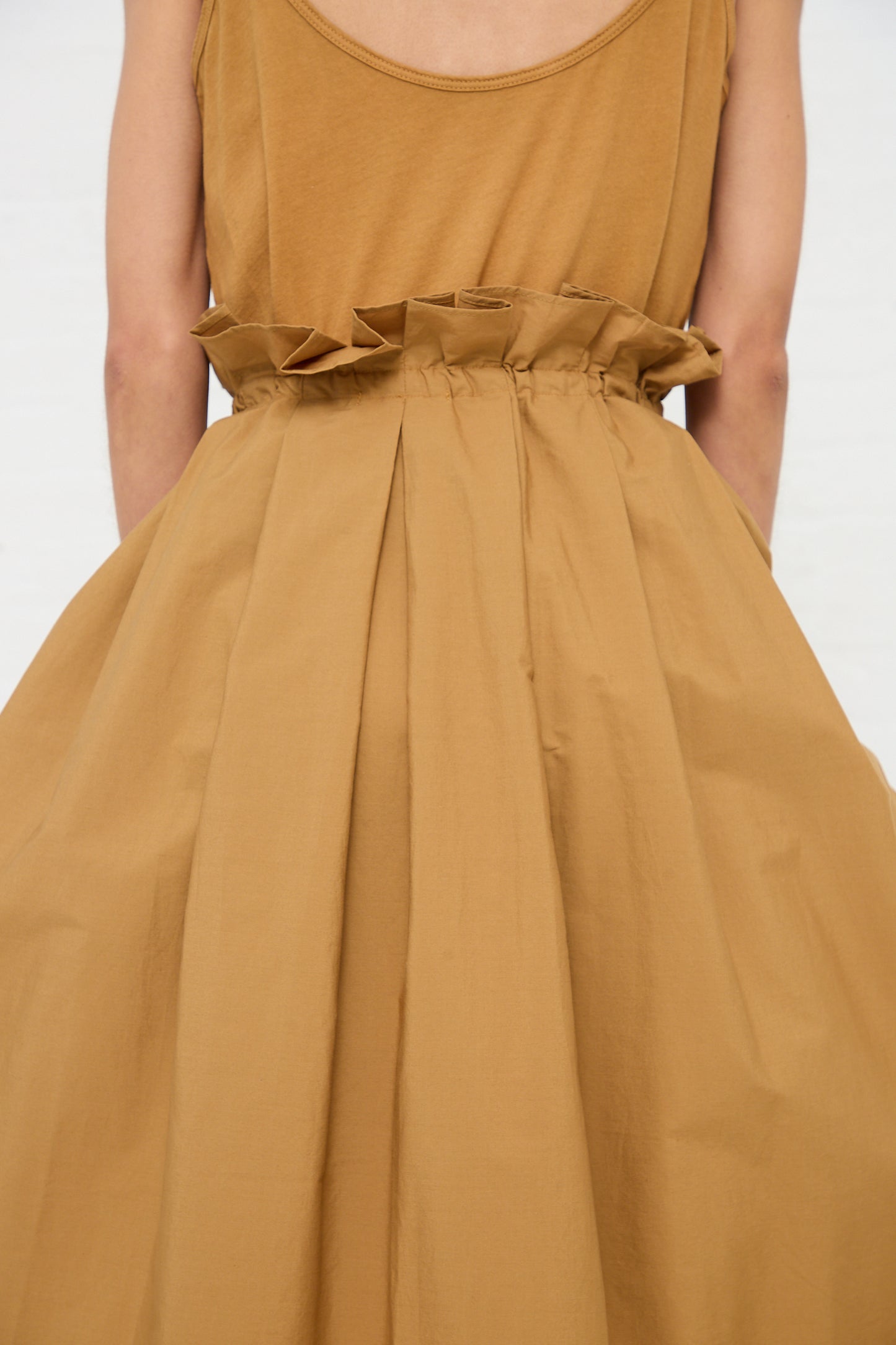 Woman wearing a tan dress with a Black Crane Cotton Parachute Skirt in Camel and a bow detail at the waist.