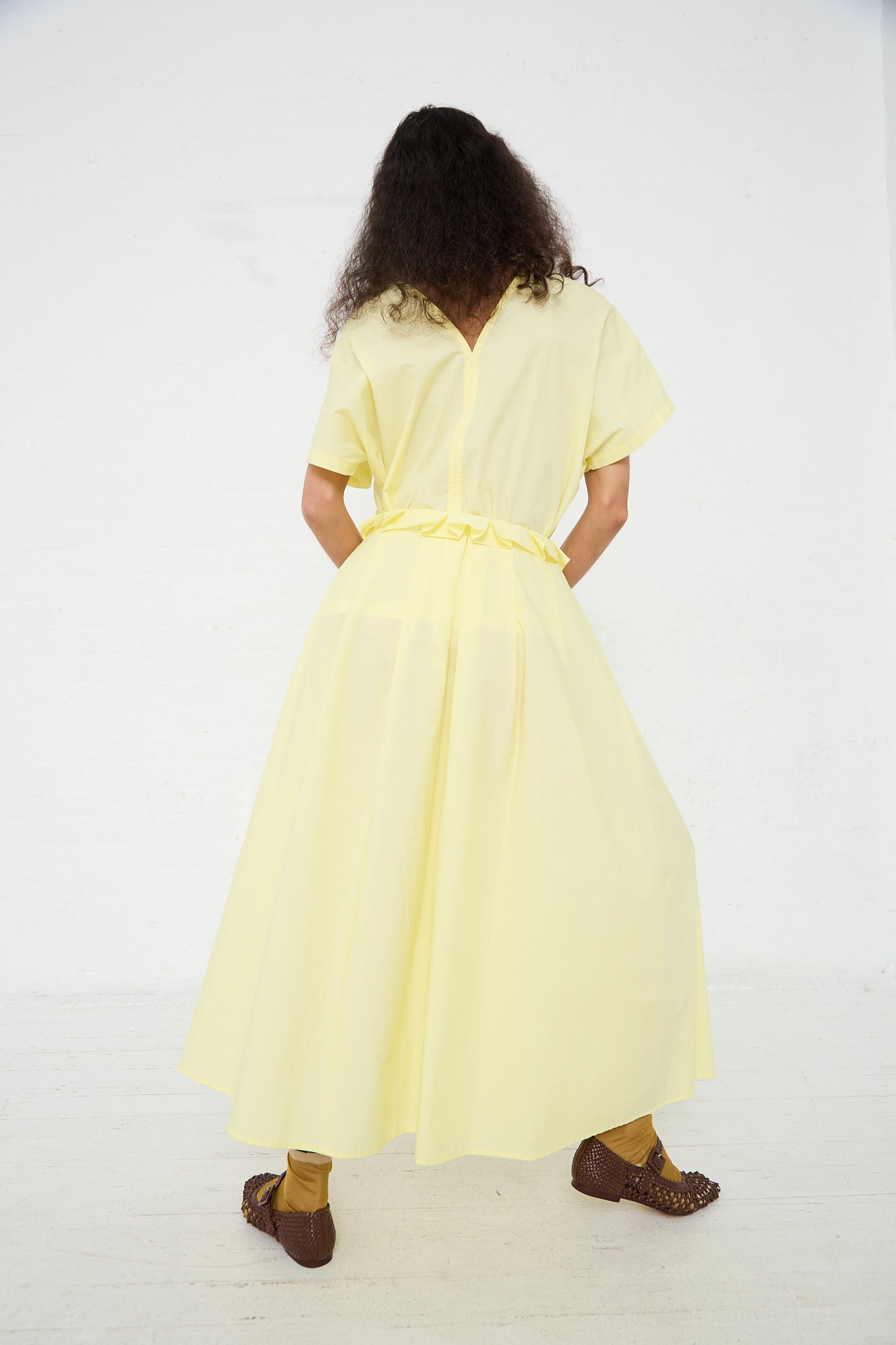 A woman seen from behind wearing a yellow mid-length dress with a Black Crane Organic Cotton Parachute Skirt in Lemon and brown ankle boots.