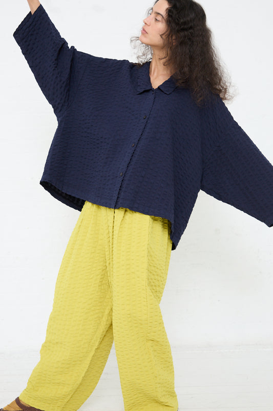 A person wearing a Black Crane Cotton Seersucker Chelsea Collar Shirt in Navy and bright yellow pants strikes a dynamic pose against a white background.