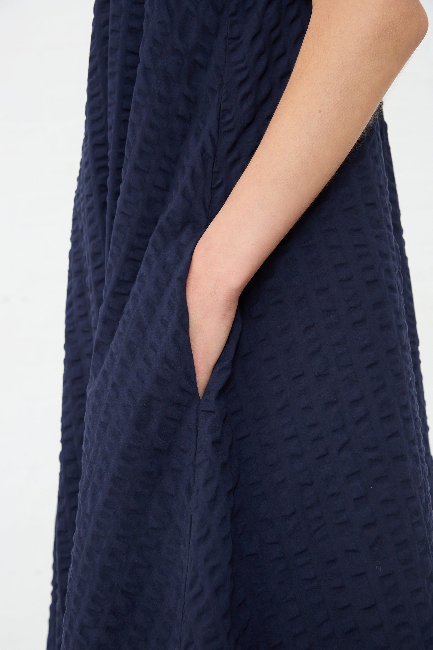 A close-up view of a person wearing a Black Crane Cotton Seersucker Parachute Dress in Navy with a visible arm seam.